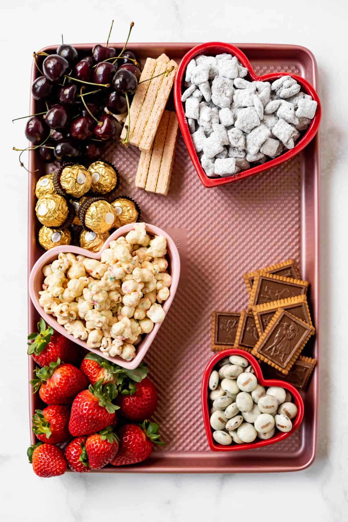 Adding fruit and large cookies and candy around heart shaped bowls to create a Valentine's Day themed dessert board.