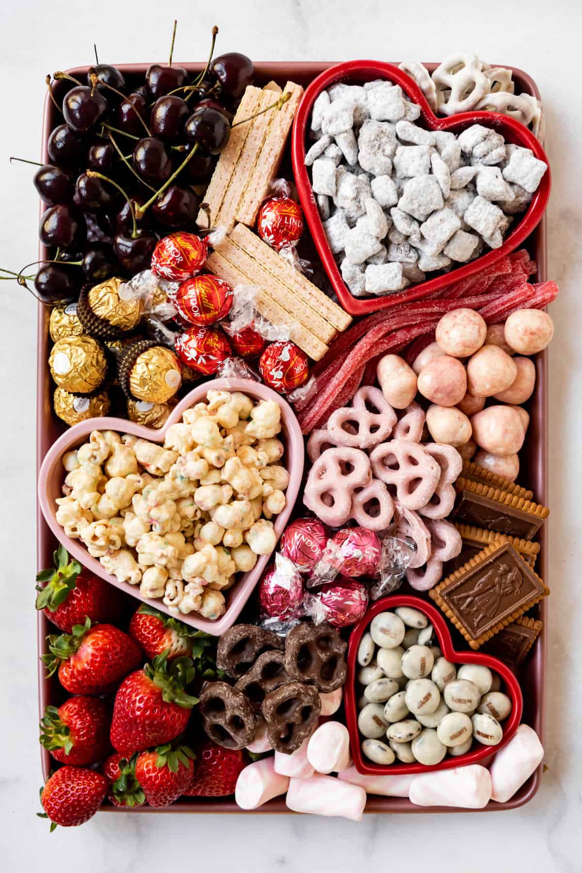 A valentine's day dessert charcuterie board with popcorn, puppy chow, strawberries, and chocolate.