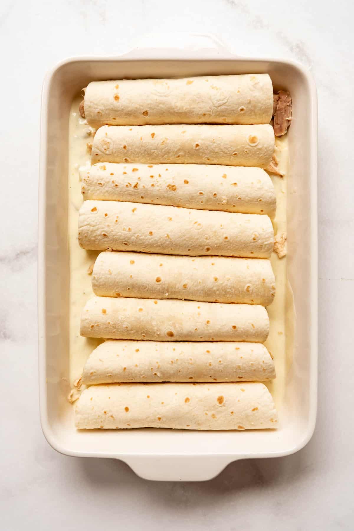 Tortillas filled with chicken and cheese rolled into enchiladas and place in a large white baking dish.