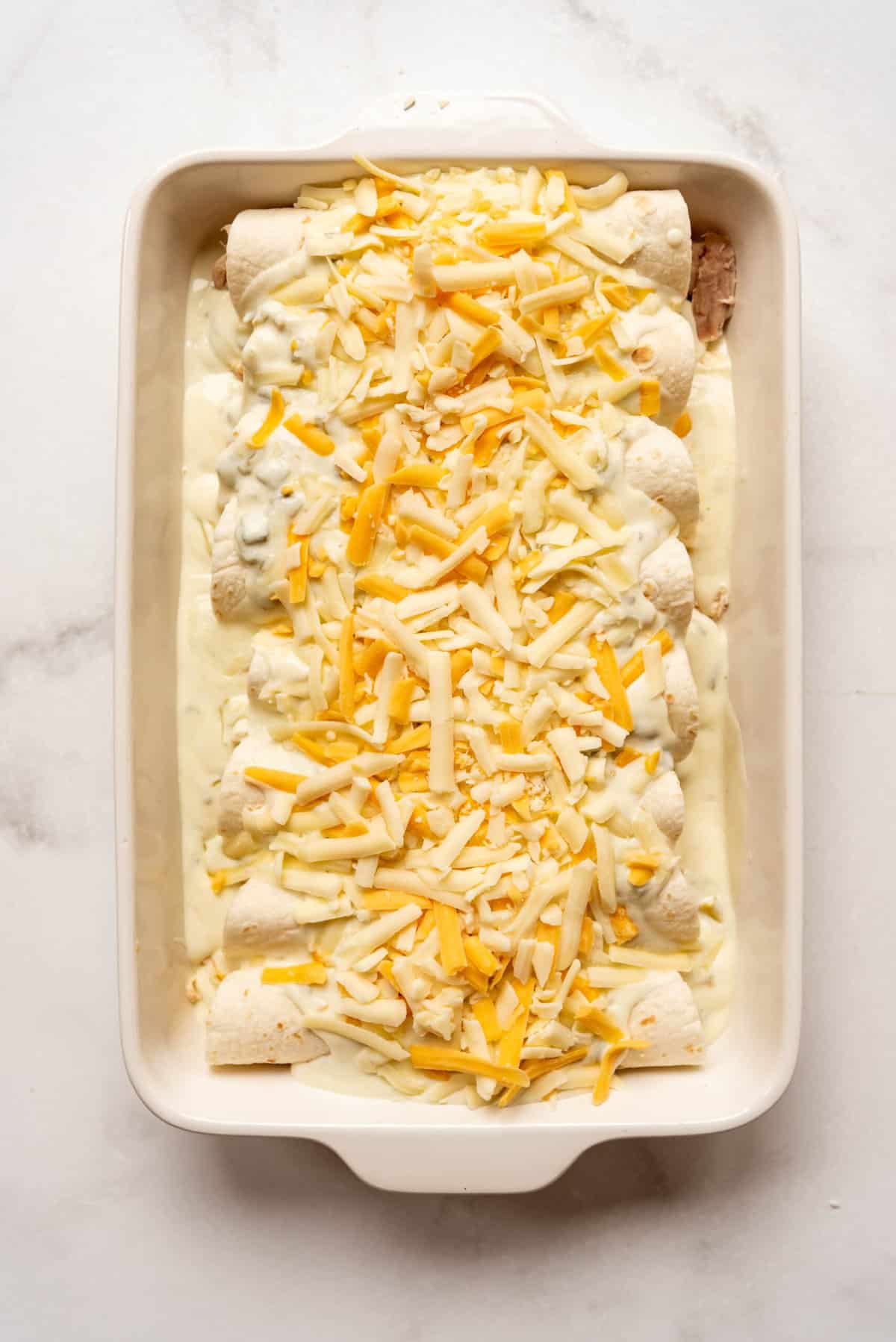 Topping chicken enchiladas with shredded cheese.