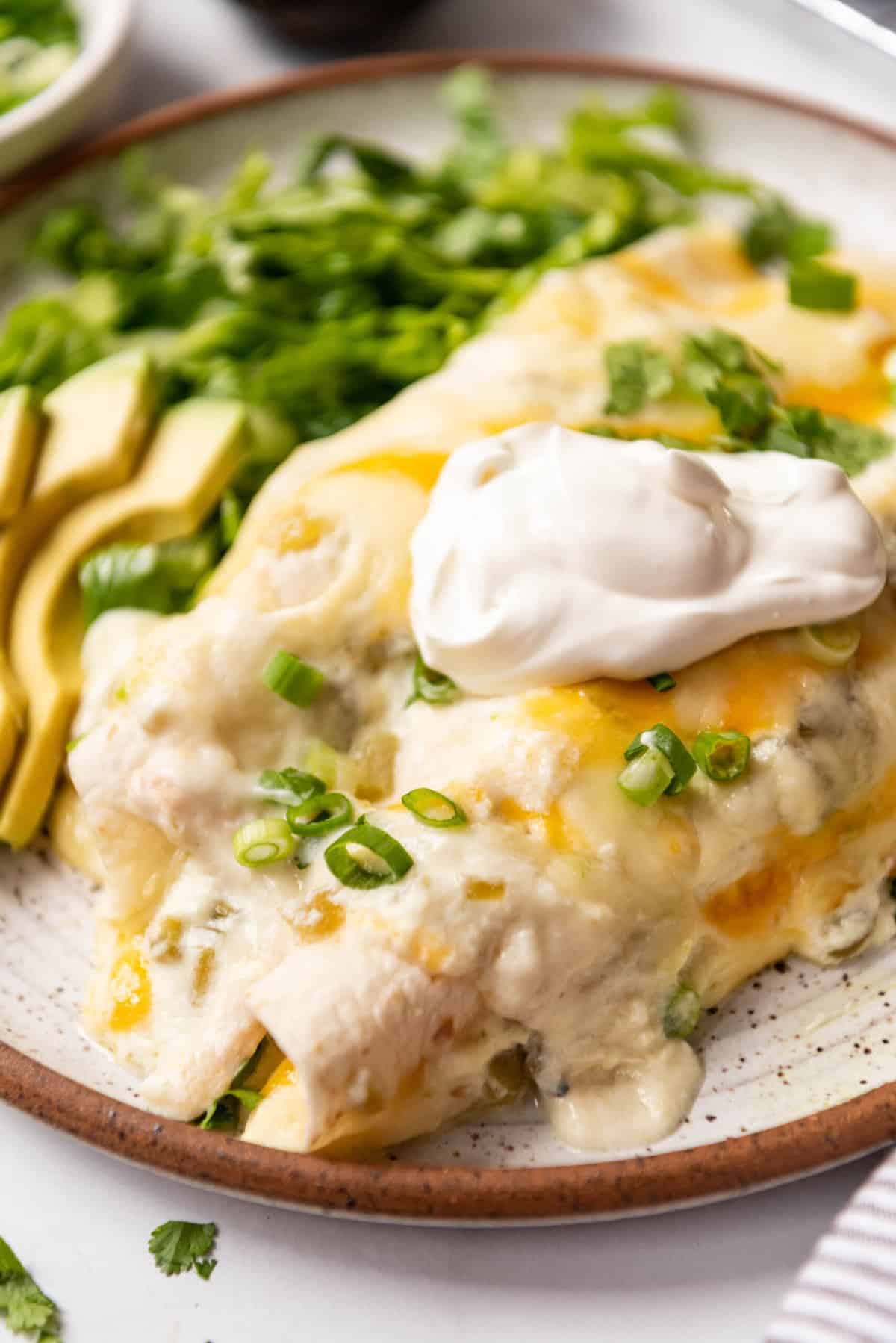Creamy white chicken enchiladas on a plate with a dollop of sour cream on top.
