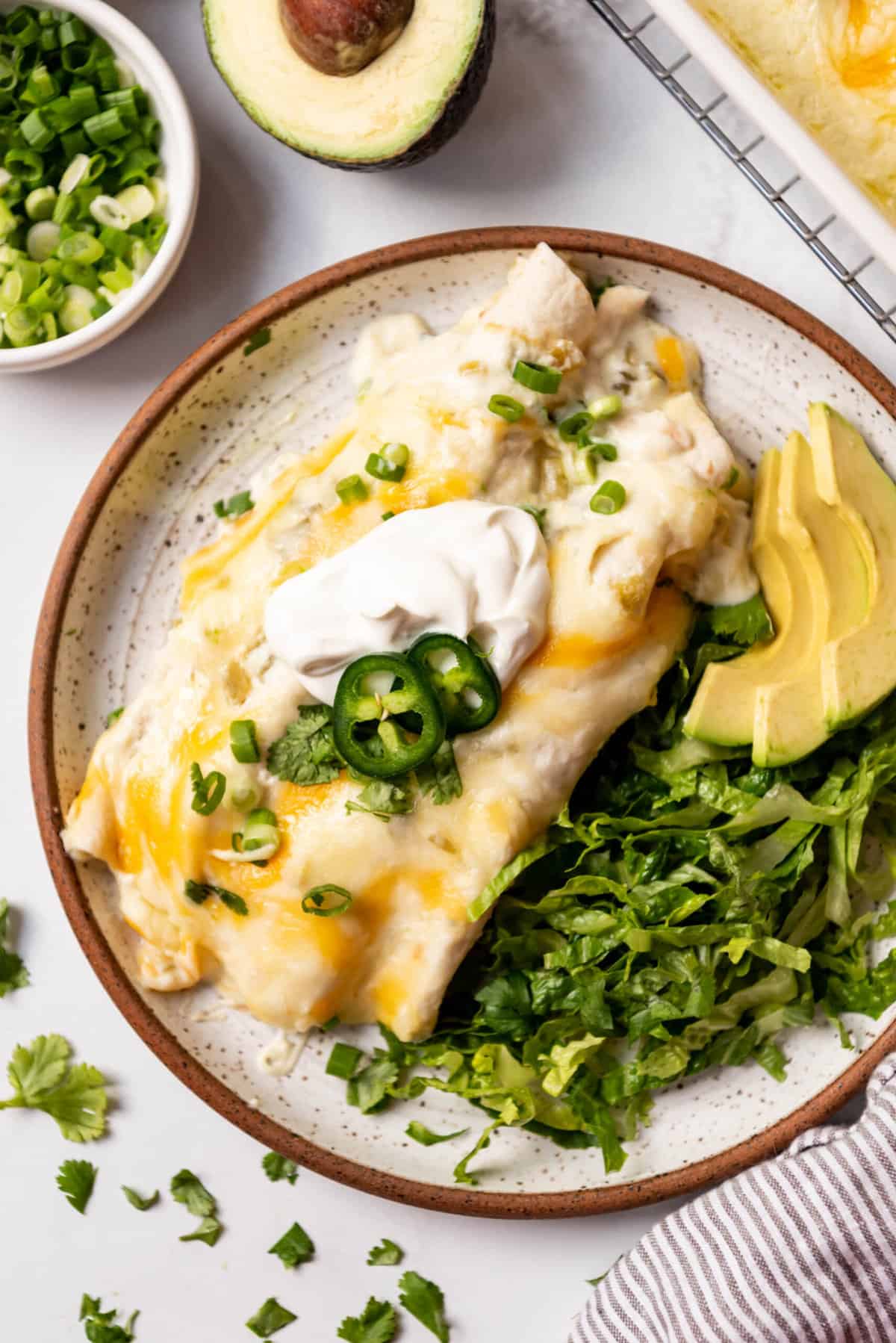 An overhead image of a plate of sour cream chicken enchiladas with lettuce and avocado on the side.