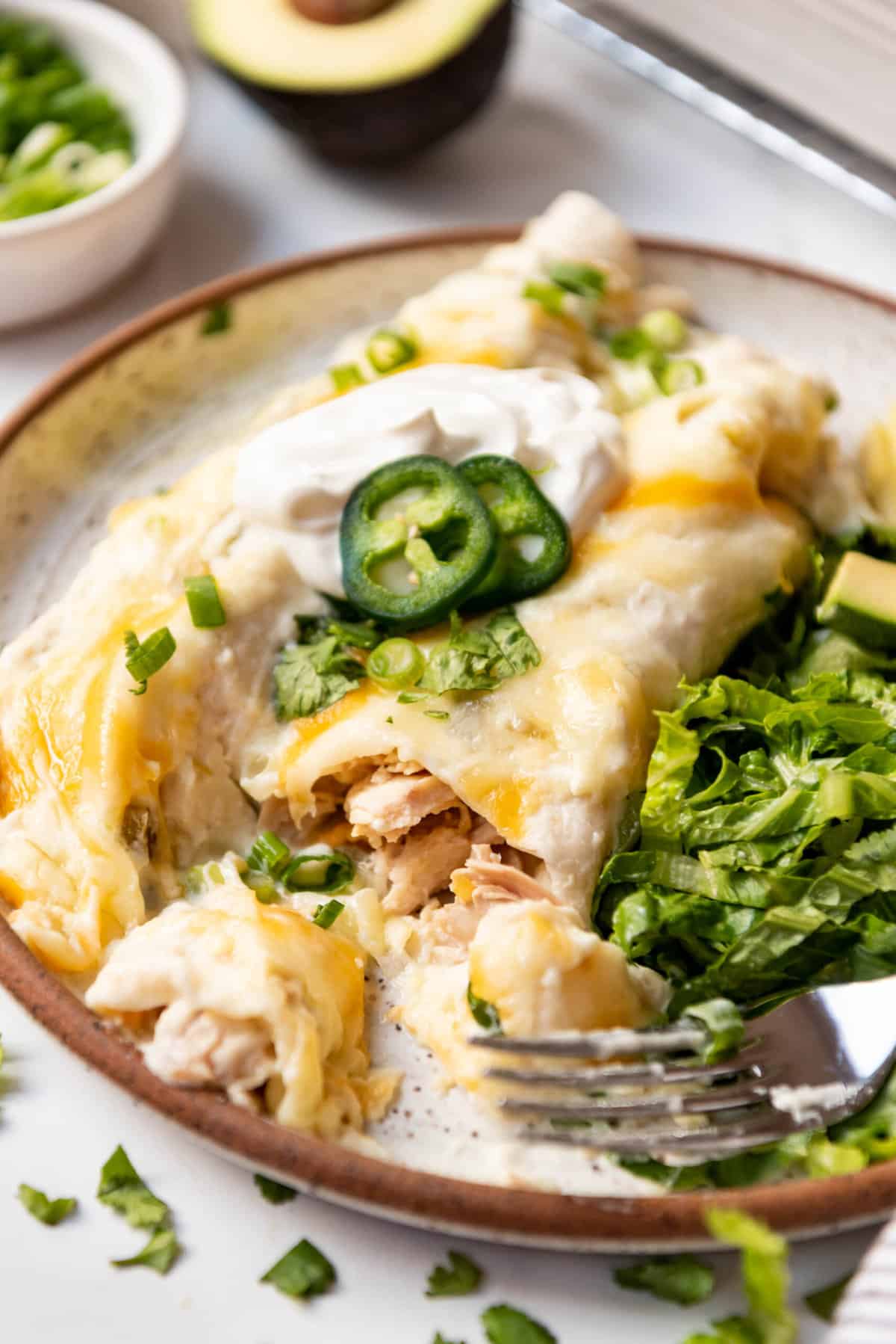 Two white chicken enchiladas on a plate with a bite taken out of one of them.