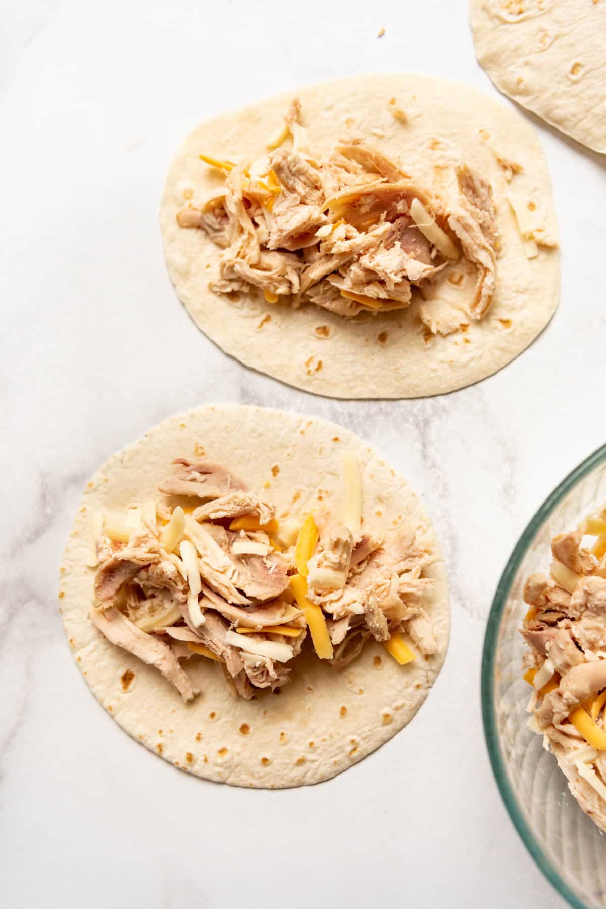 Tortillas piled with shredded chicken and cheese.