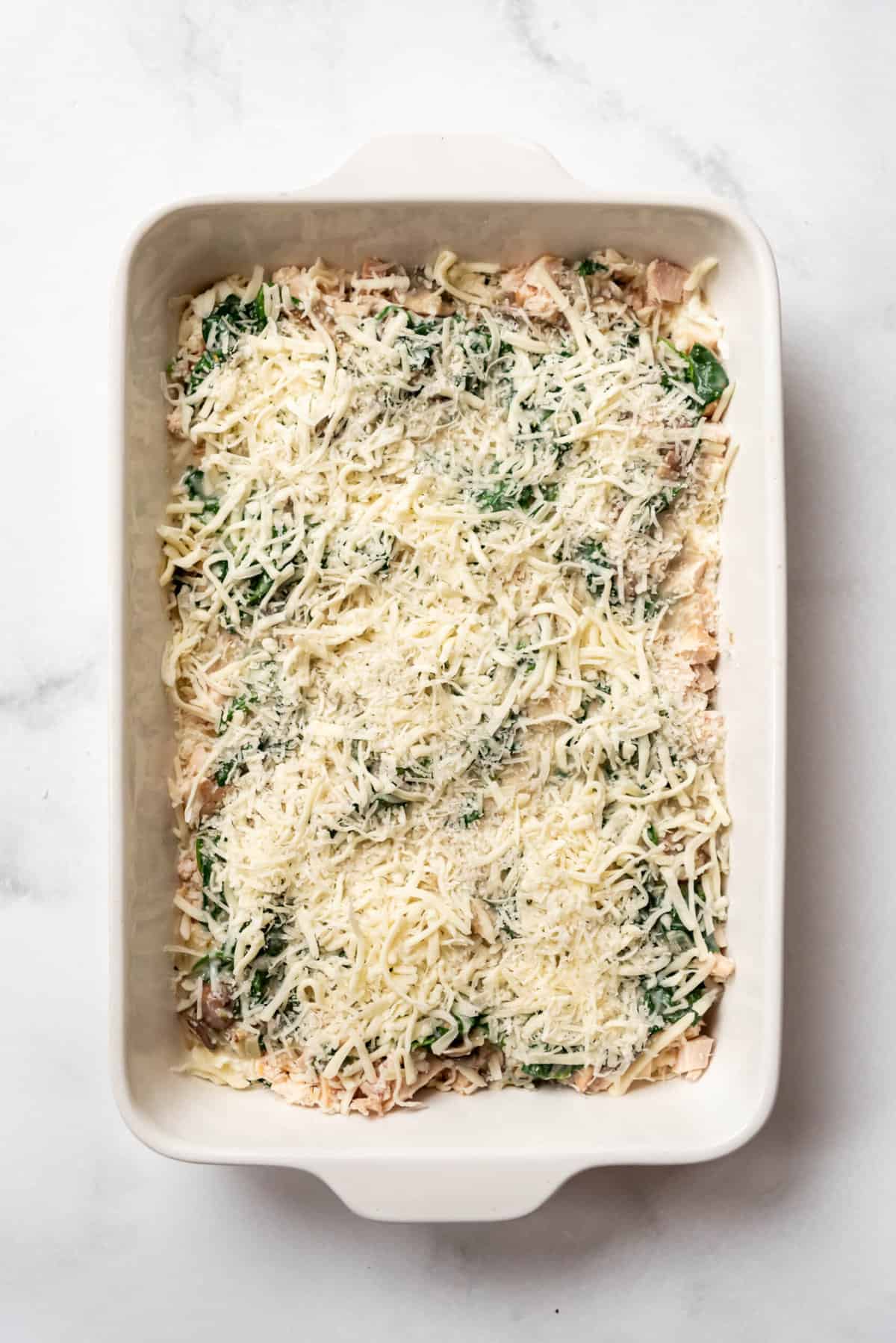 Sprinkling mozzarella and parmesan cheese over lasagna layers in a white casserole dish.