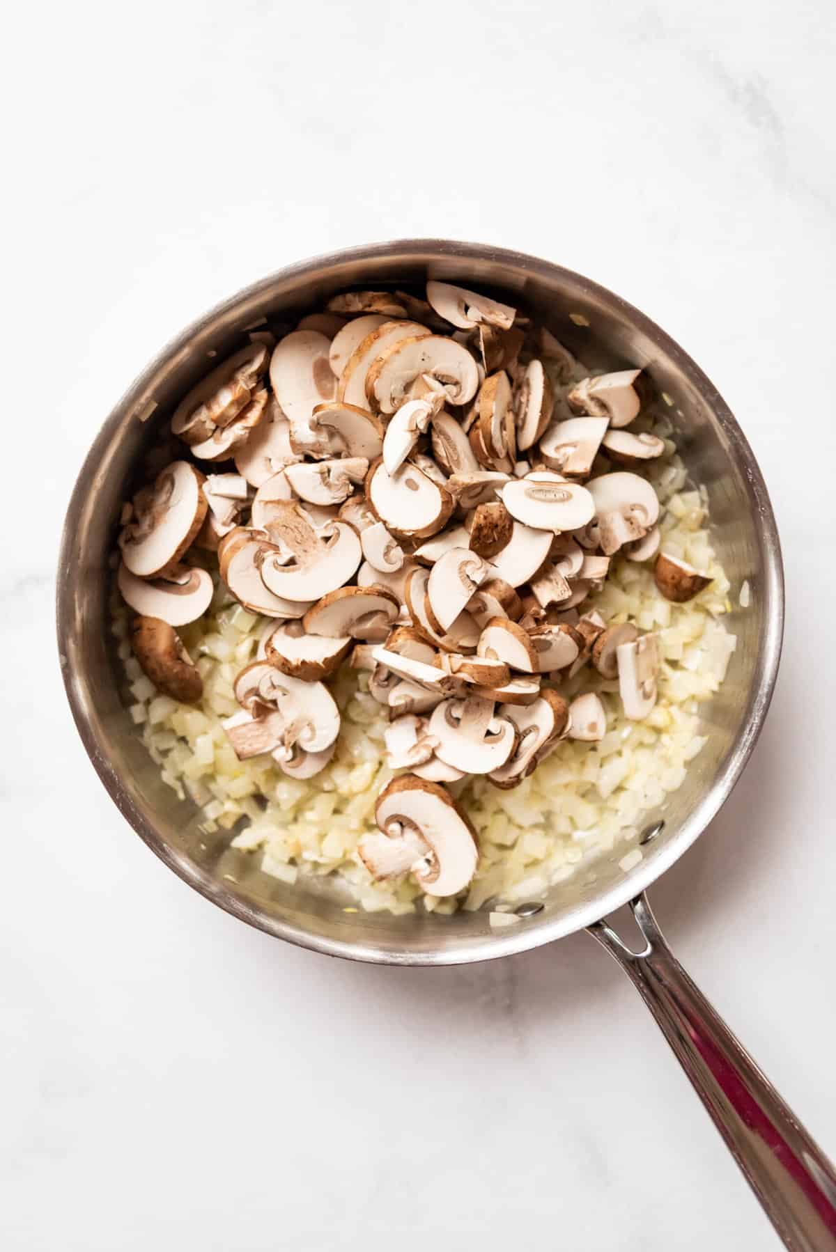Adding sliced mushrooms to a pan with sauteed onions.