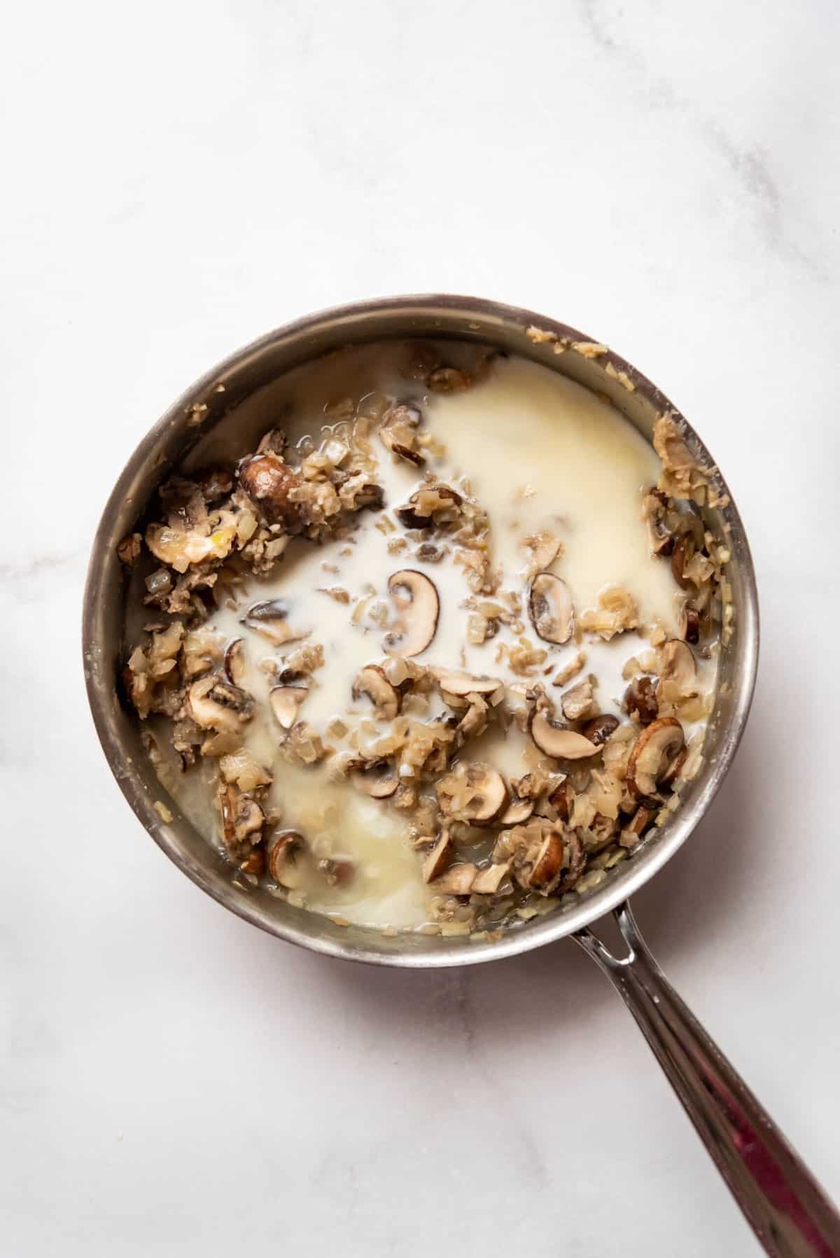 Adding chicken broth and cream to sauteed onions and mushrooms in a pan.