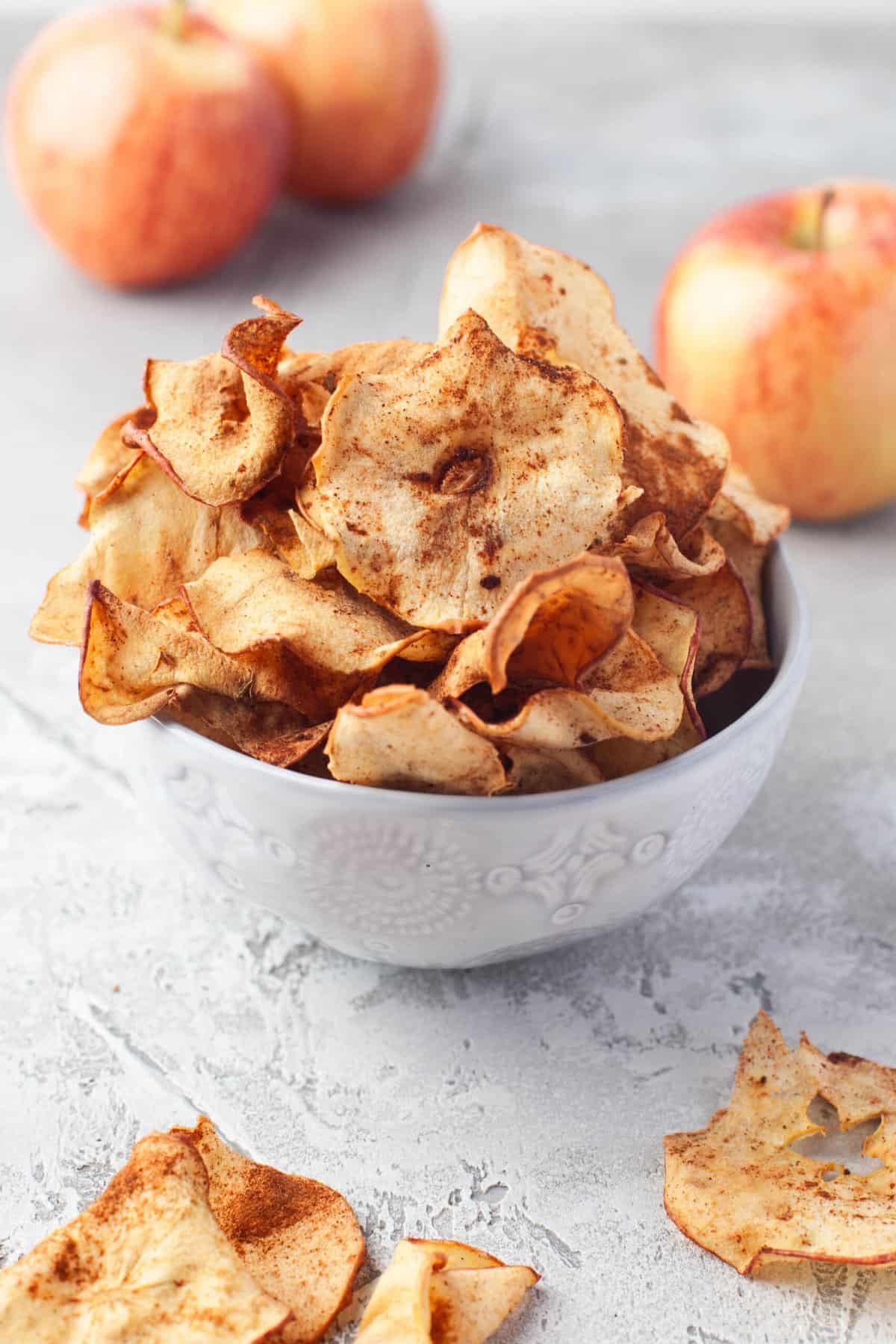 A bowl of apple chips in front of gala apples.