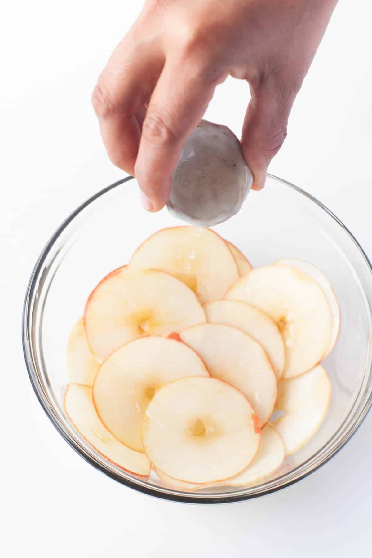 Adding melted coconut oil to thinly sliced apples.