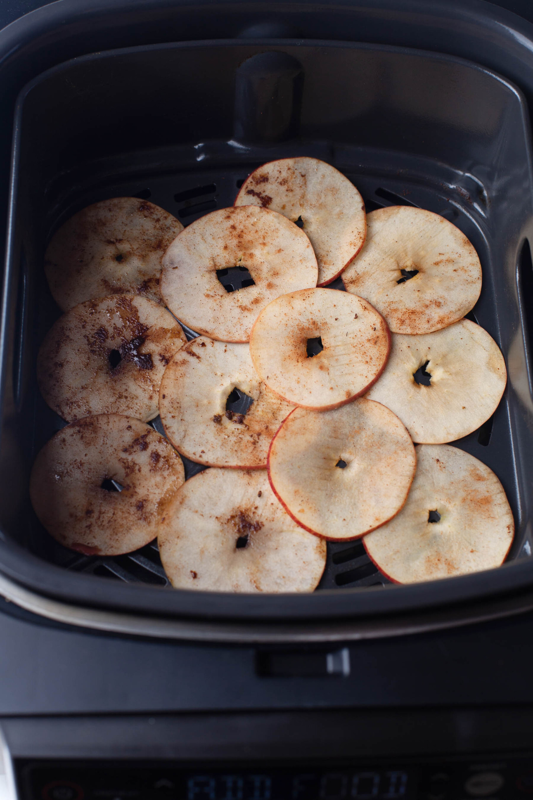 Adding thinly sliced apples in an evenly layer in an air fryer.