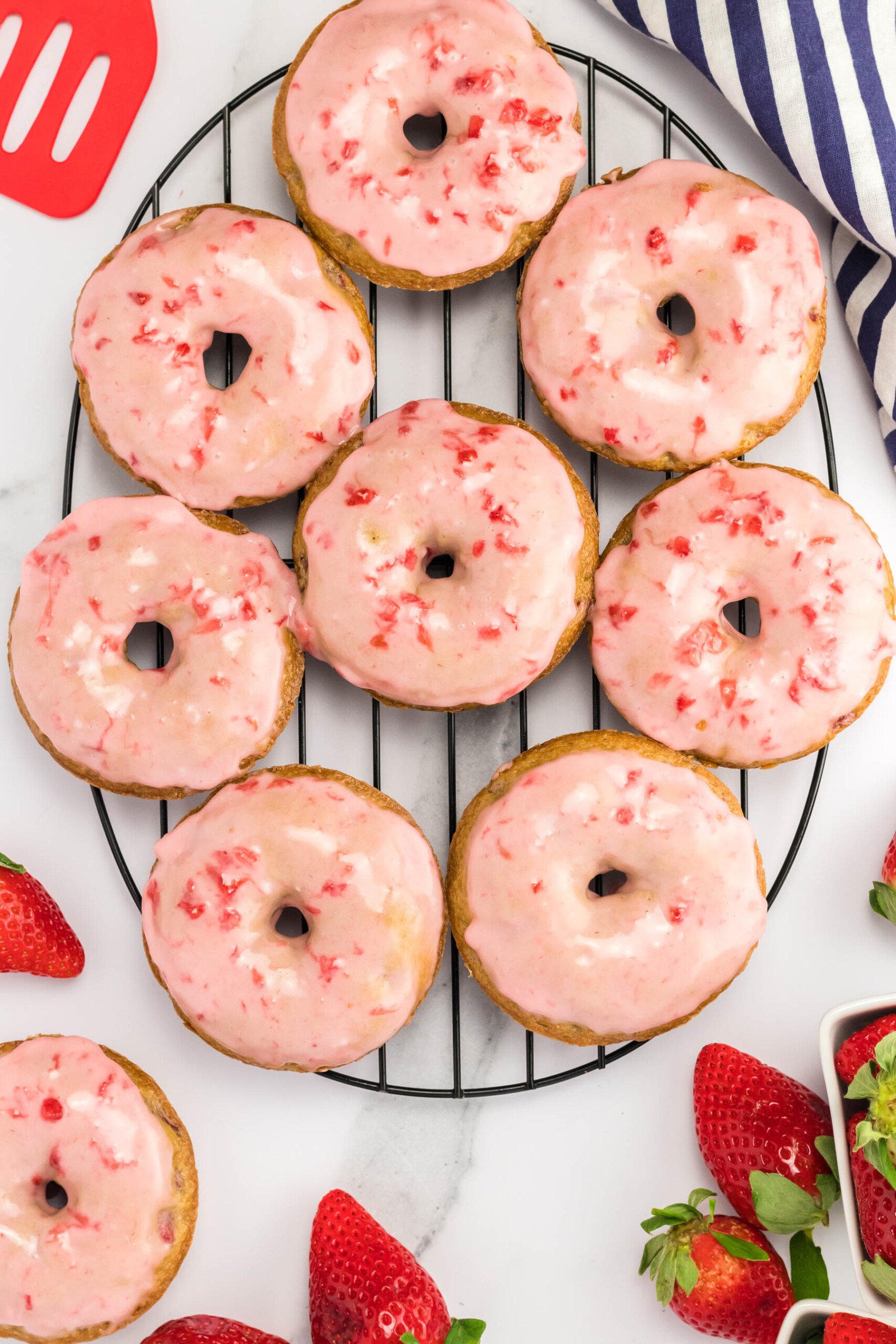 Top view of freshly glazed strawberry donuts on a wire rack. 
