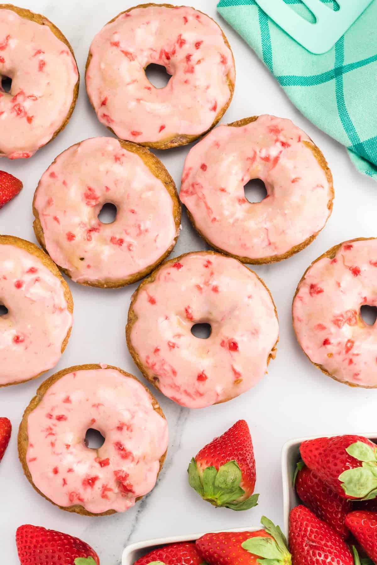 Baked strawberry donuts next to fresh strawberries.