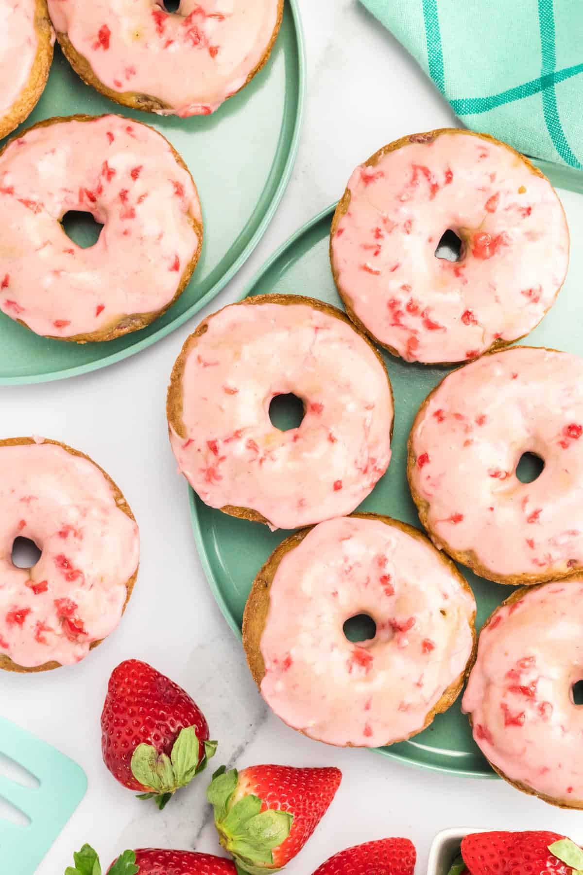 Top view of baked strawberry donuts on a work top next to fresh strawberries. 