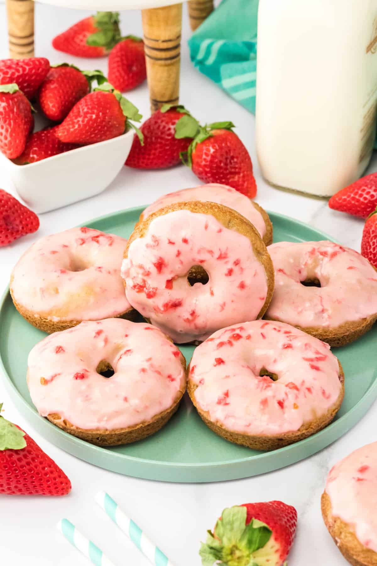 A blue plate filled with strawberry donuts next to a glass of milk. 