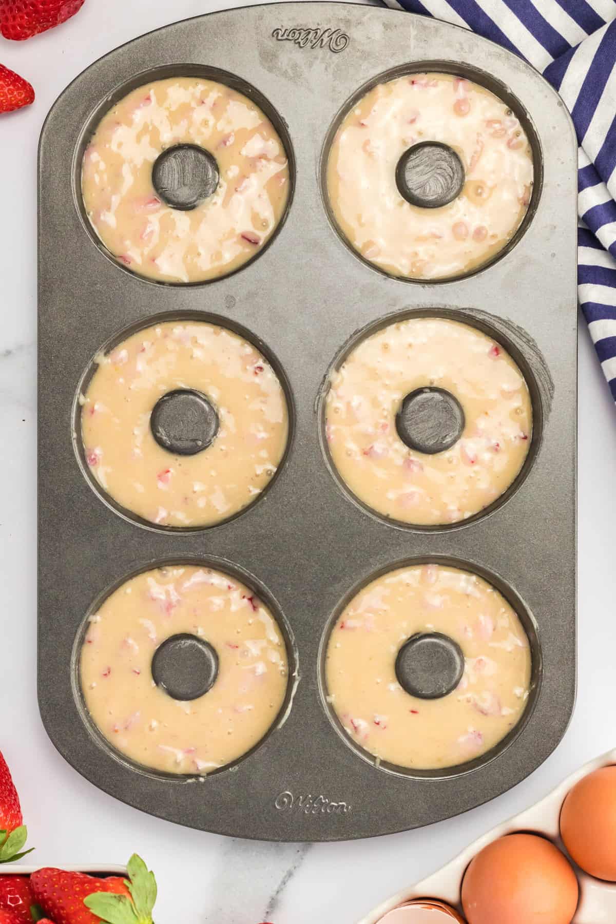 Top view of donut baking pan with strawberry donut batter filling the donut rings. 