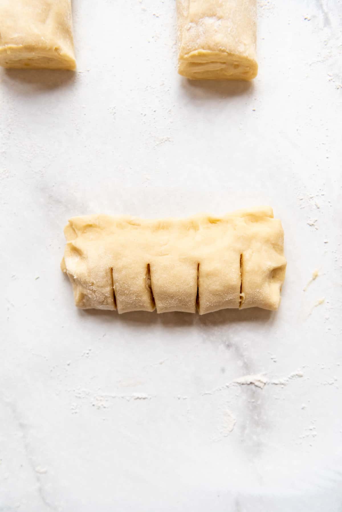 Slicing slits into bear claw dough and pinches the edges closed.