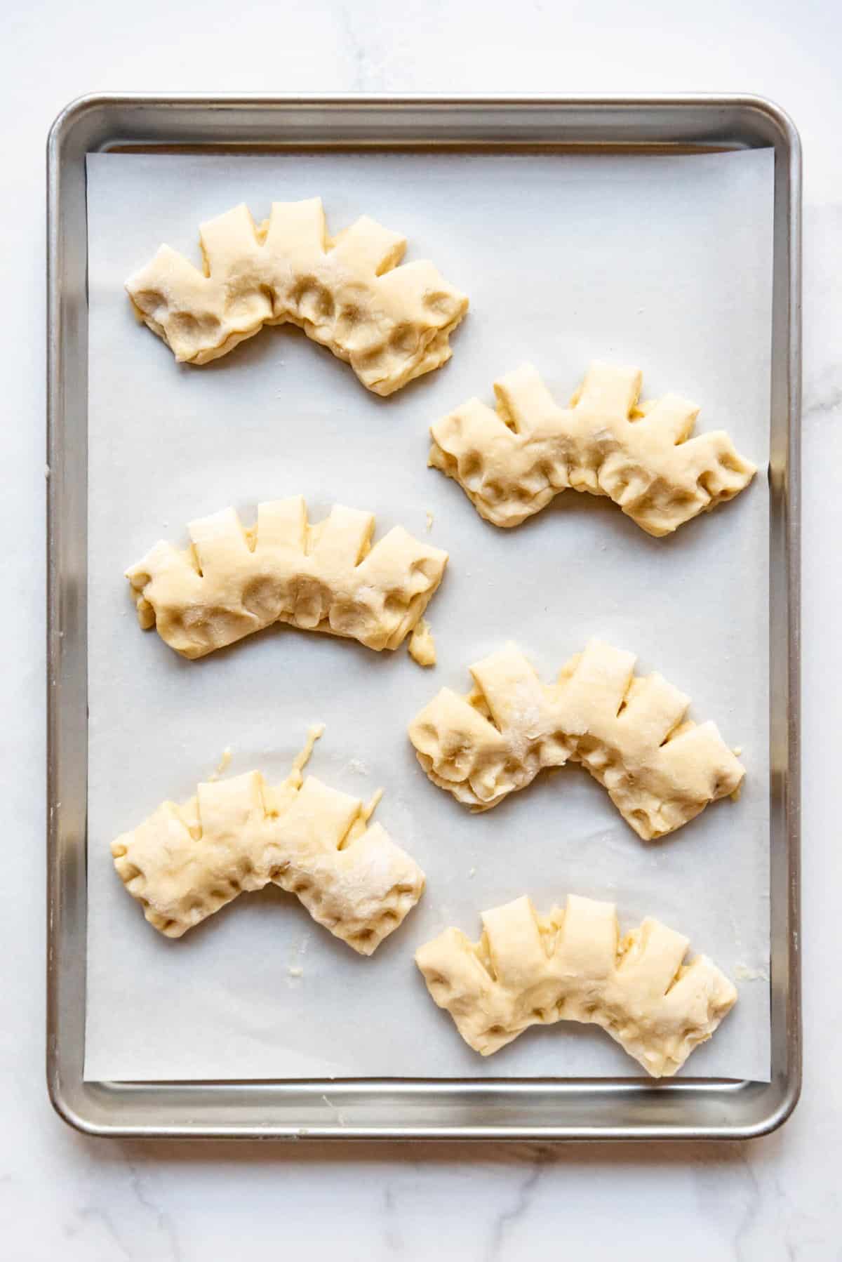 Shaped bear claw pastries on a baking sheet lined with parchment paper.