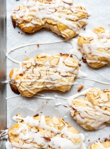 Glazed bear claw pastries on a baking sheet with sliced almonds on top.