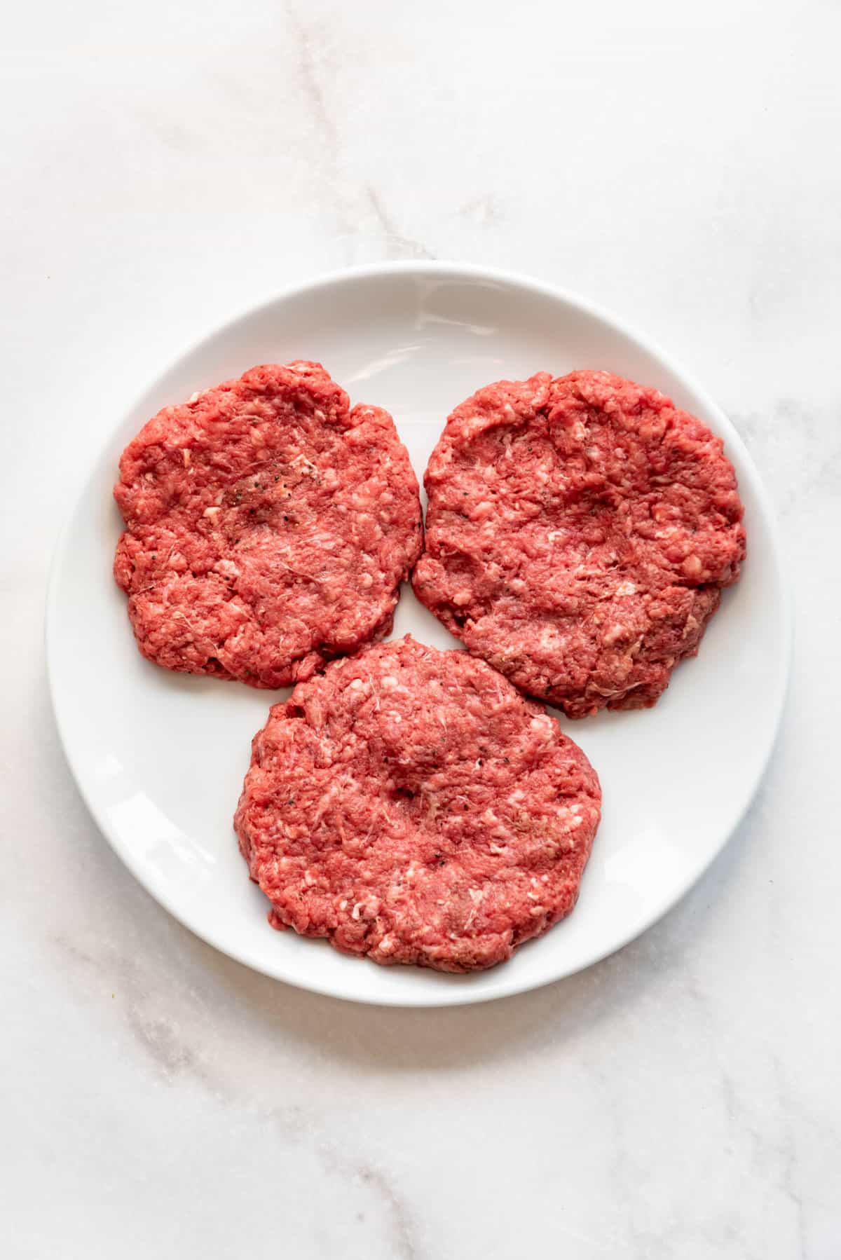 Shaping ground bison into burger patties on a white plate.