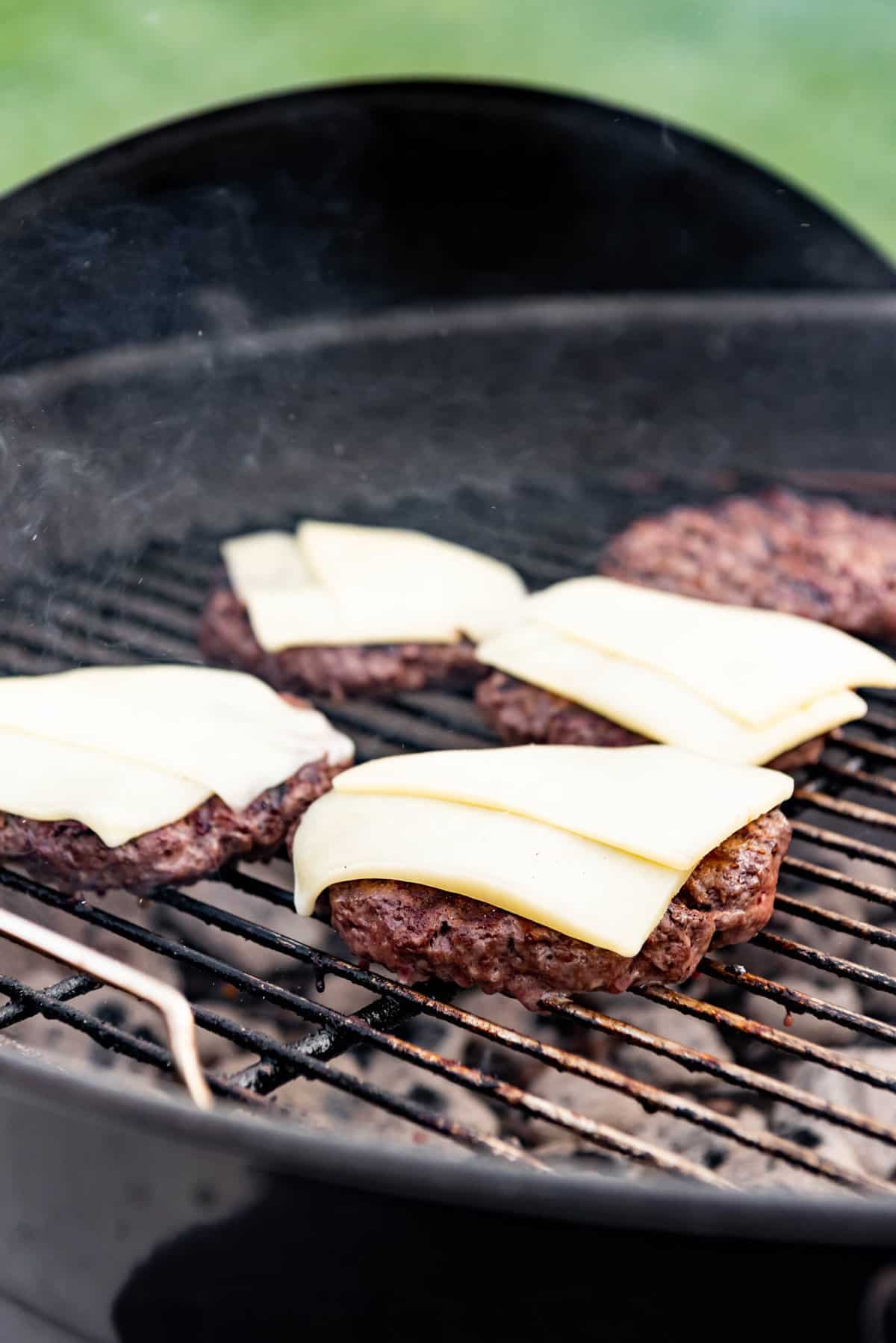 Adding cheese slices to burgers on the grill.