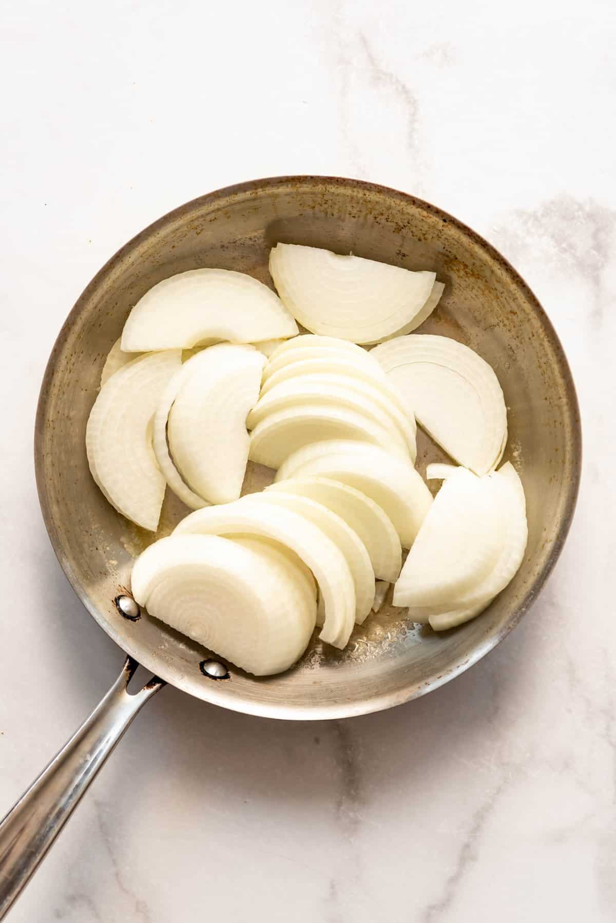 Adding sliced onions to a large skillet with melted butter.