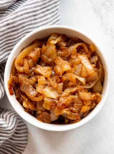 Caramelized onions in a white bowl next to a striped cloth napkin.