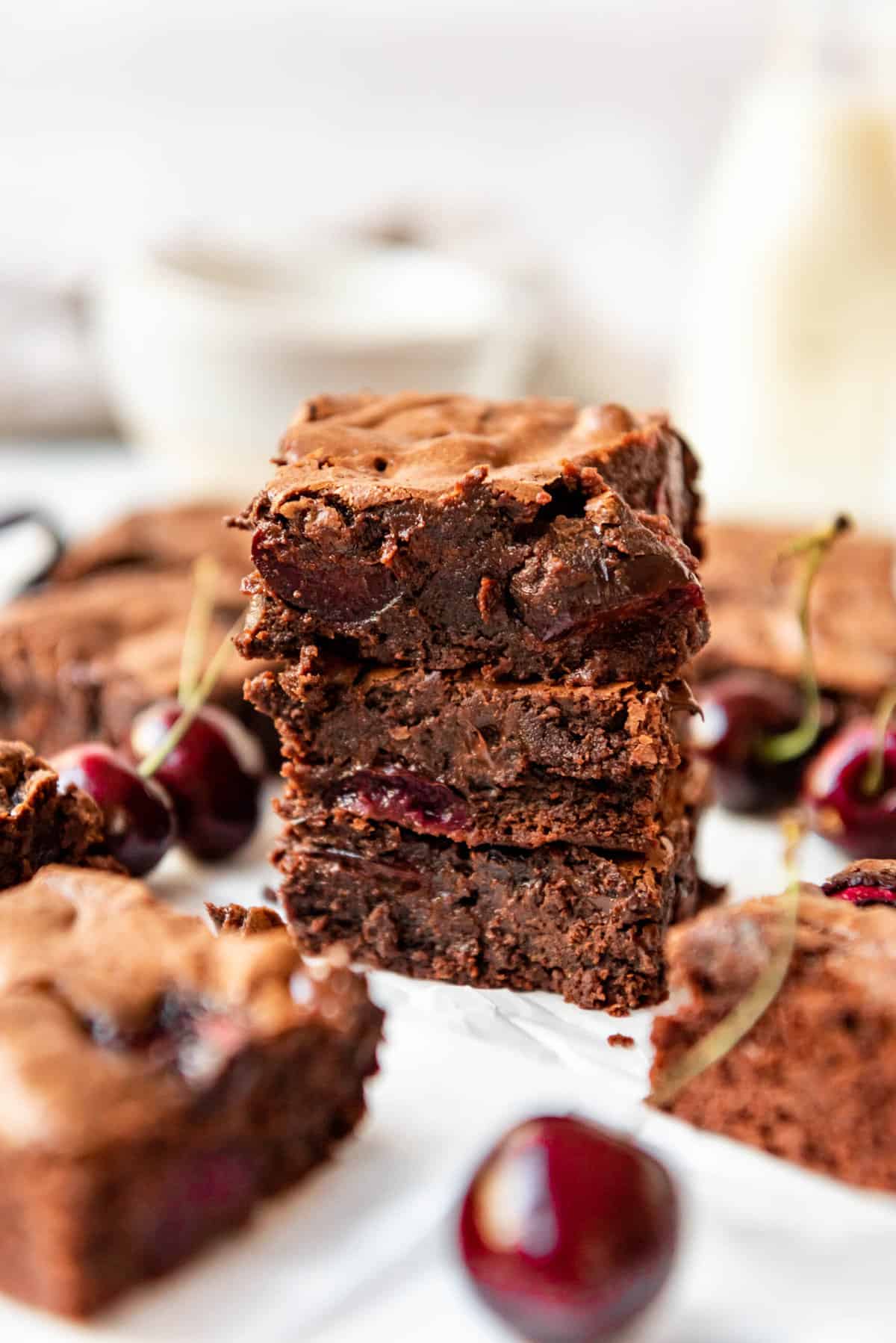 A stack of three cherry brownies with more brownies and fresh bing cherries nearby.