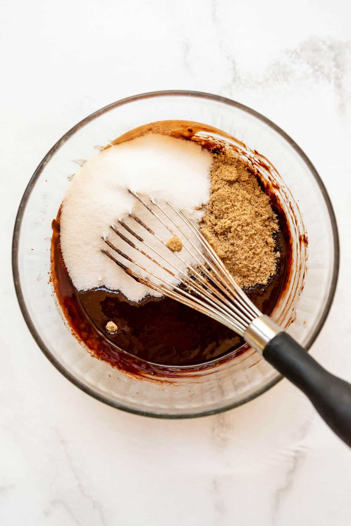 Adding granulated sugar and brown sugar to brownie batter in a large mixing bowl with a whisk.