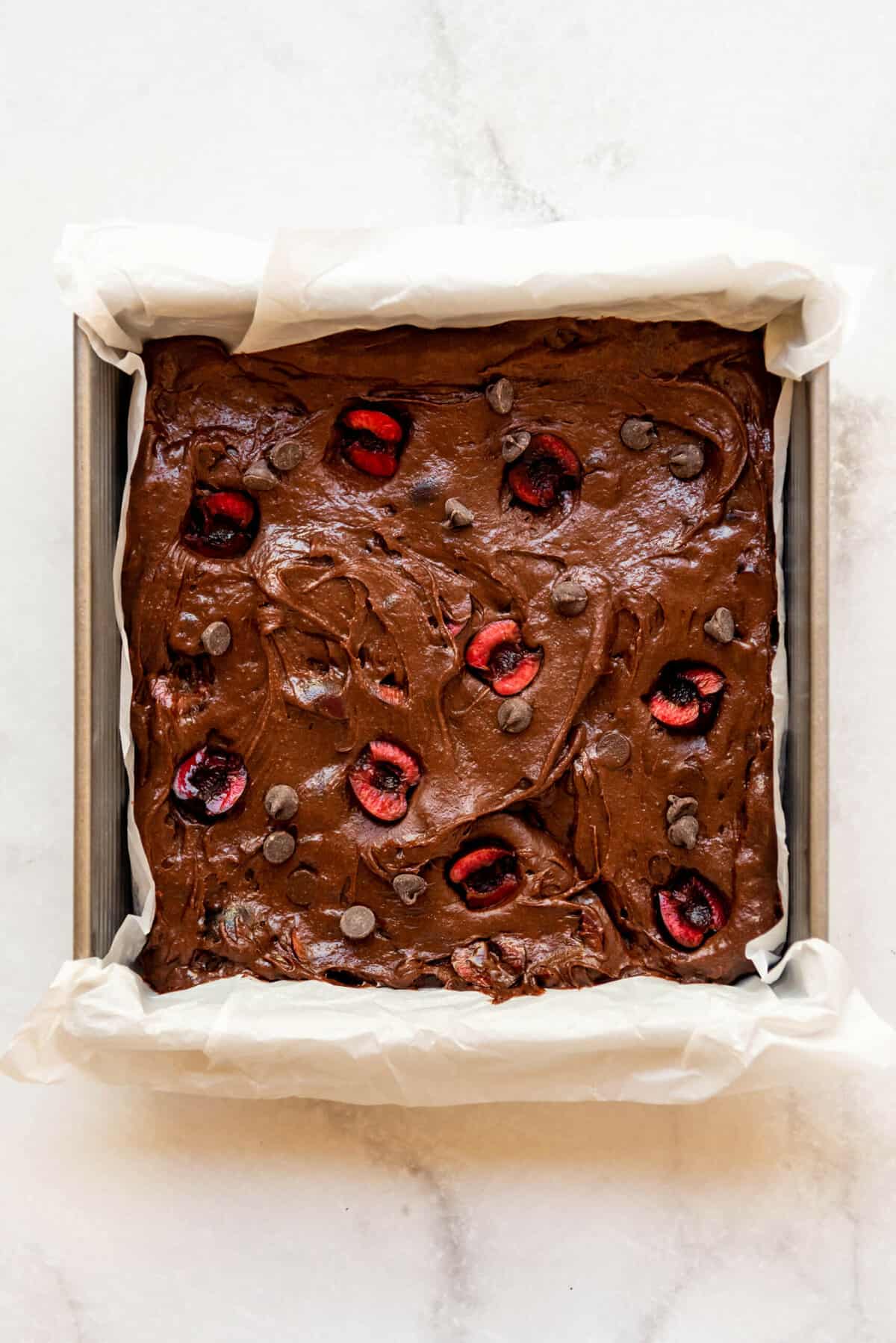 Brownie batter in a pan with fresh cherry halves pressed into the top of them.