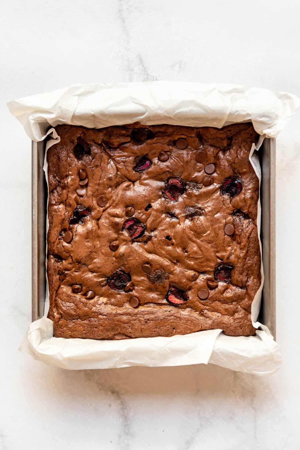 Baked cherry brownies in a pan lined with parchment paper.