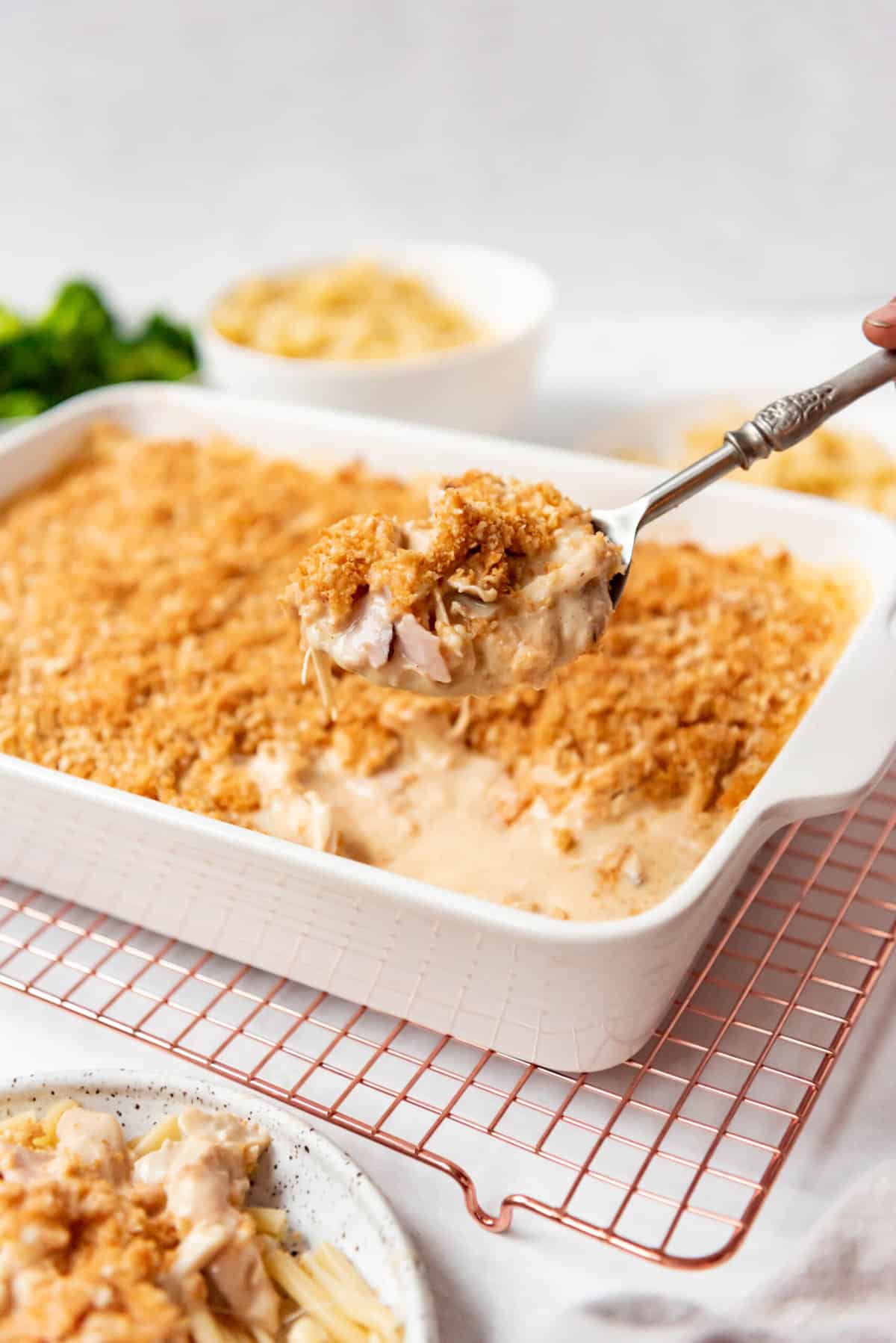 A serving spoon lifting up a spoonful of cordon bleu casserole in front of the baking dish.