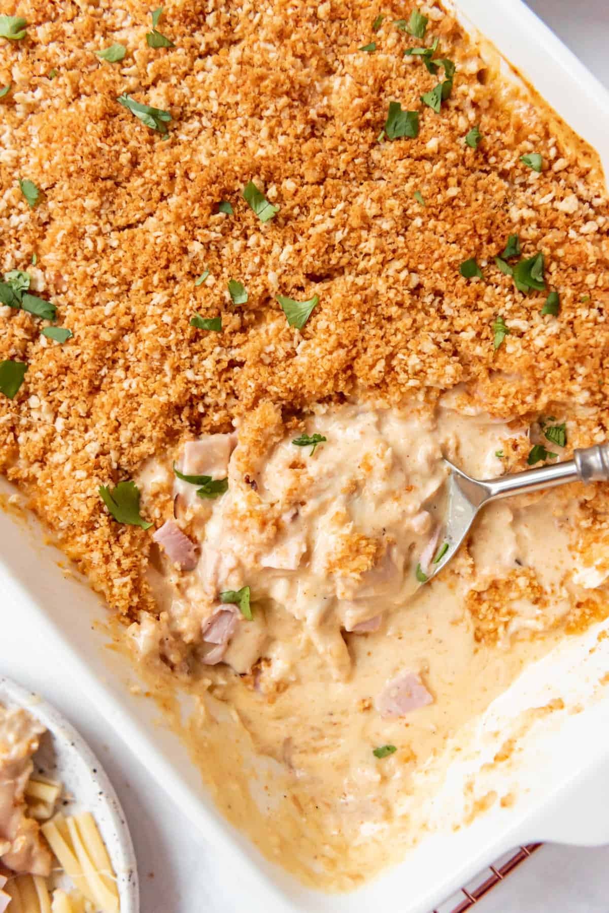 A chicken casserole with part of it scooped out showing a creamy sauce under crispy breadcrumb topping.
