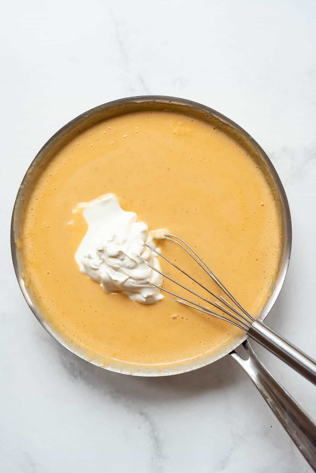 Adding sour cream to a cheesy sauce for a casserole dish.