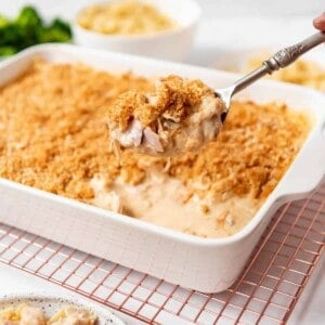 A serving spoon lifting a scoop of chicken cordon bleu casserole from a white baking dish.