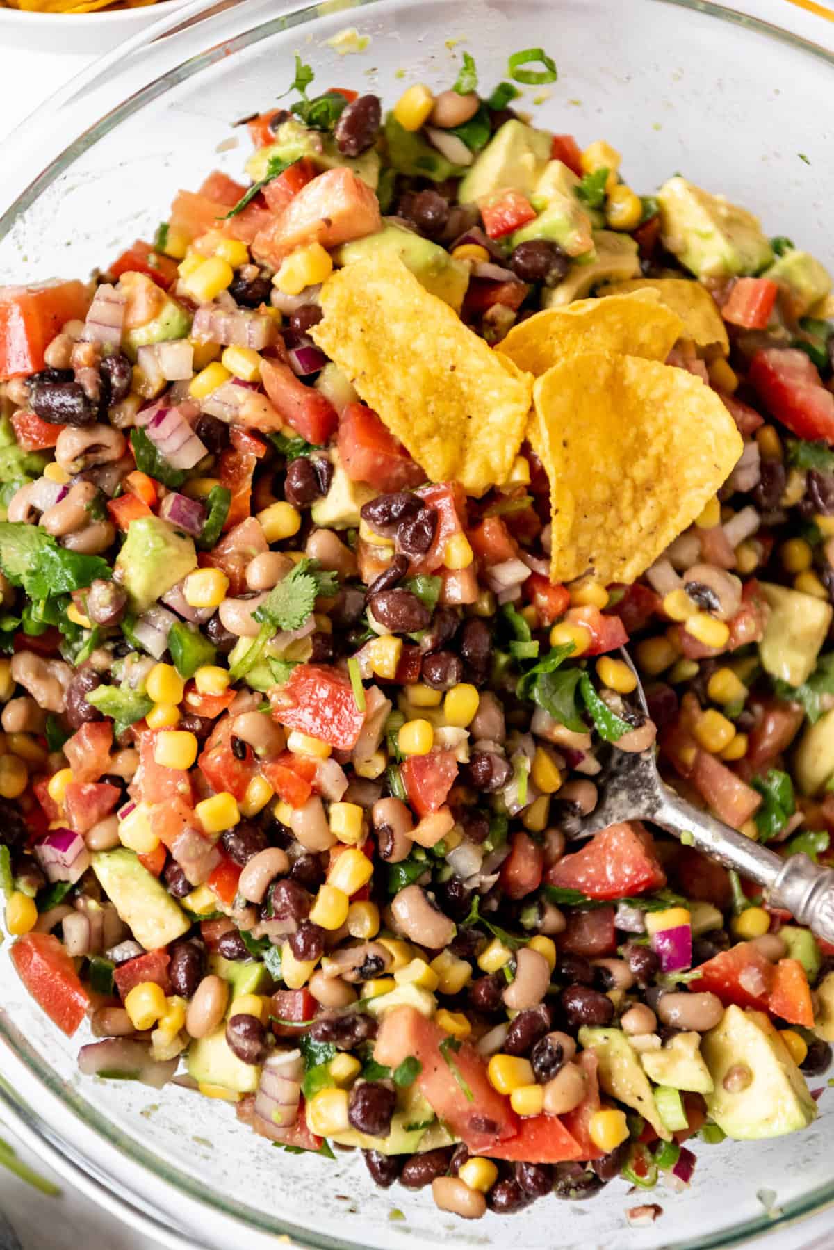 A close overhead image of a bowl of cowboy caviar with tortilla chips and a serving spoon in it.