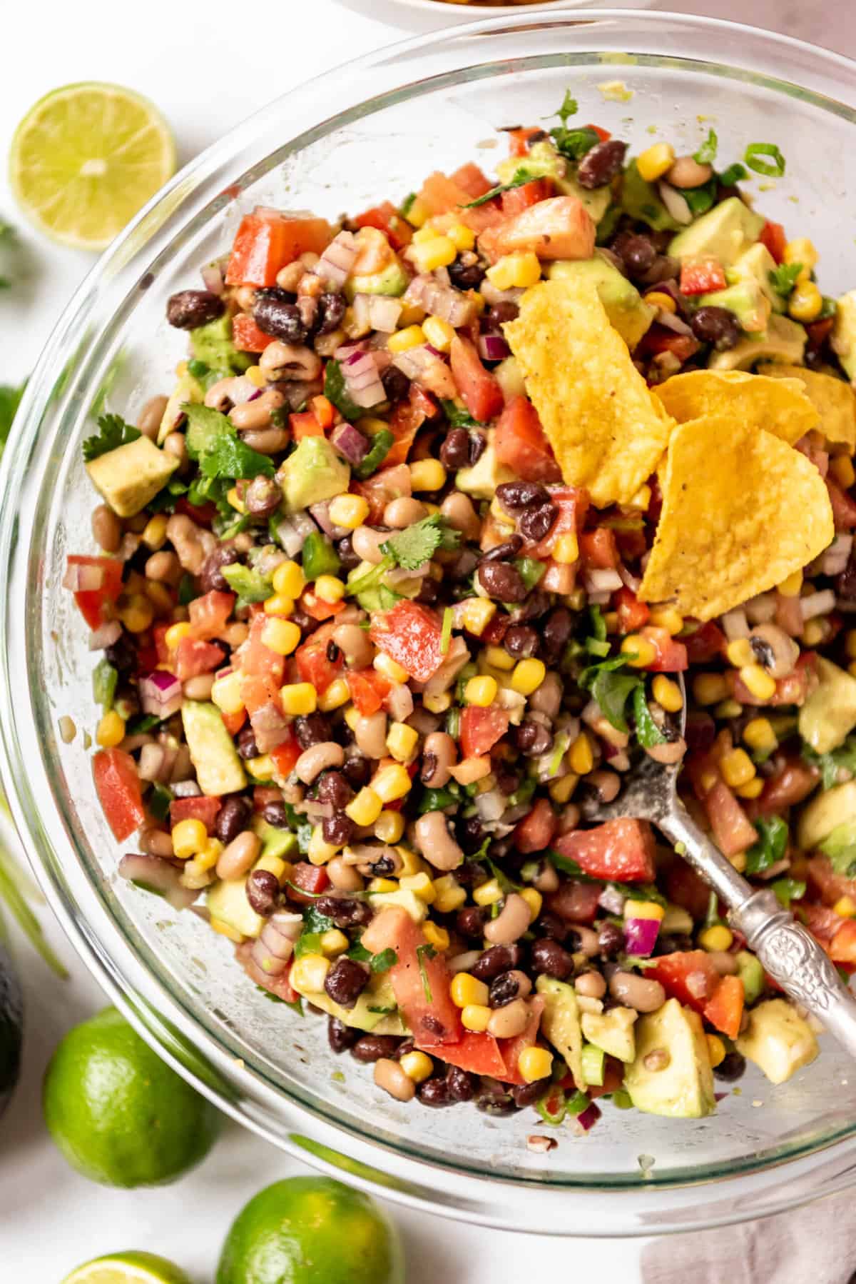 An overhead image of a serving spoon in a large bowl of cowboy caviar with a few tortilla chips in it.