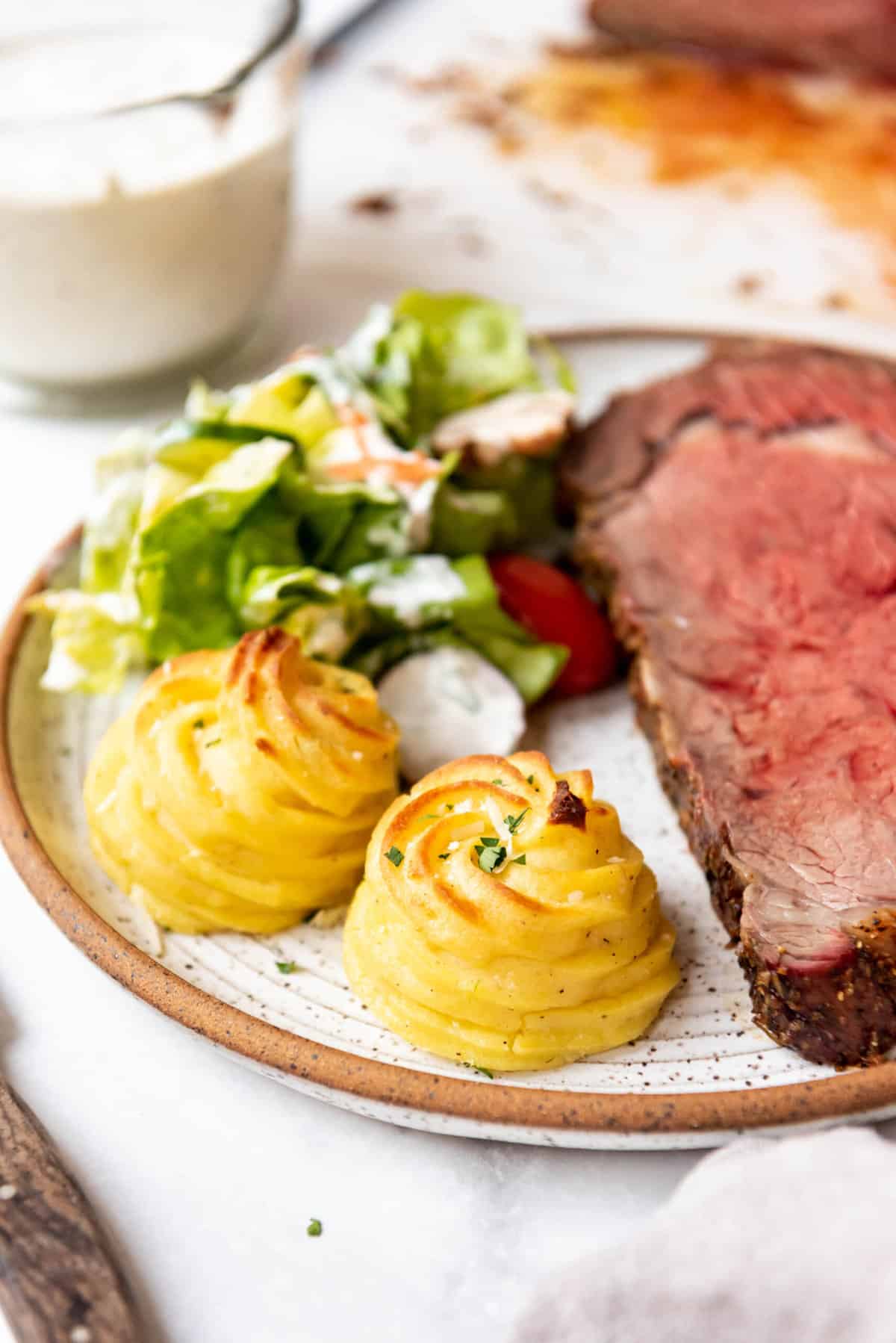A plate of prime rib, garden salad, and duchess potatoes.