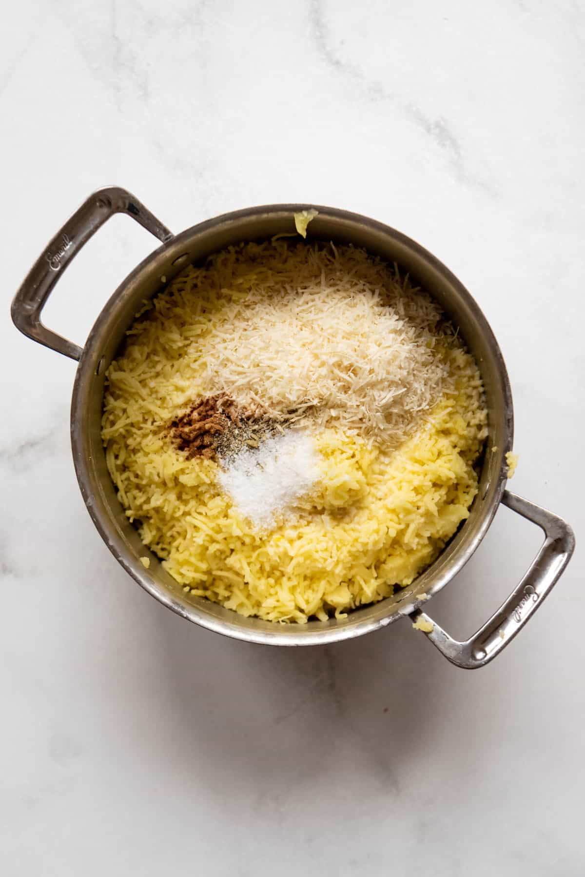 Adding freshly grated Parmesan cheese, nutmeg, salt, butter, and milk to mashed potatoes.