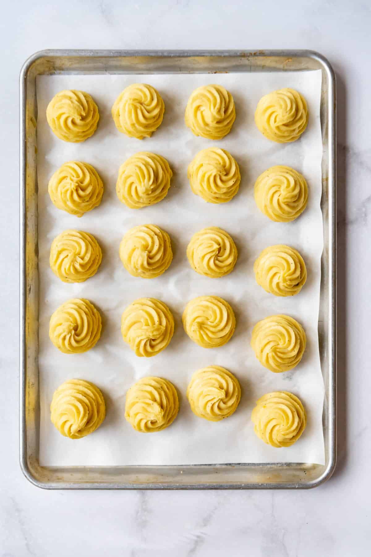Mashed potatoes piped into swirled mounds on a baking sheet lined with parchment paper.