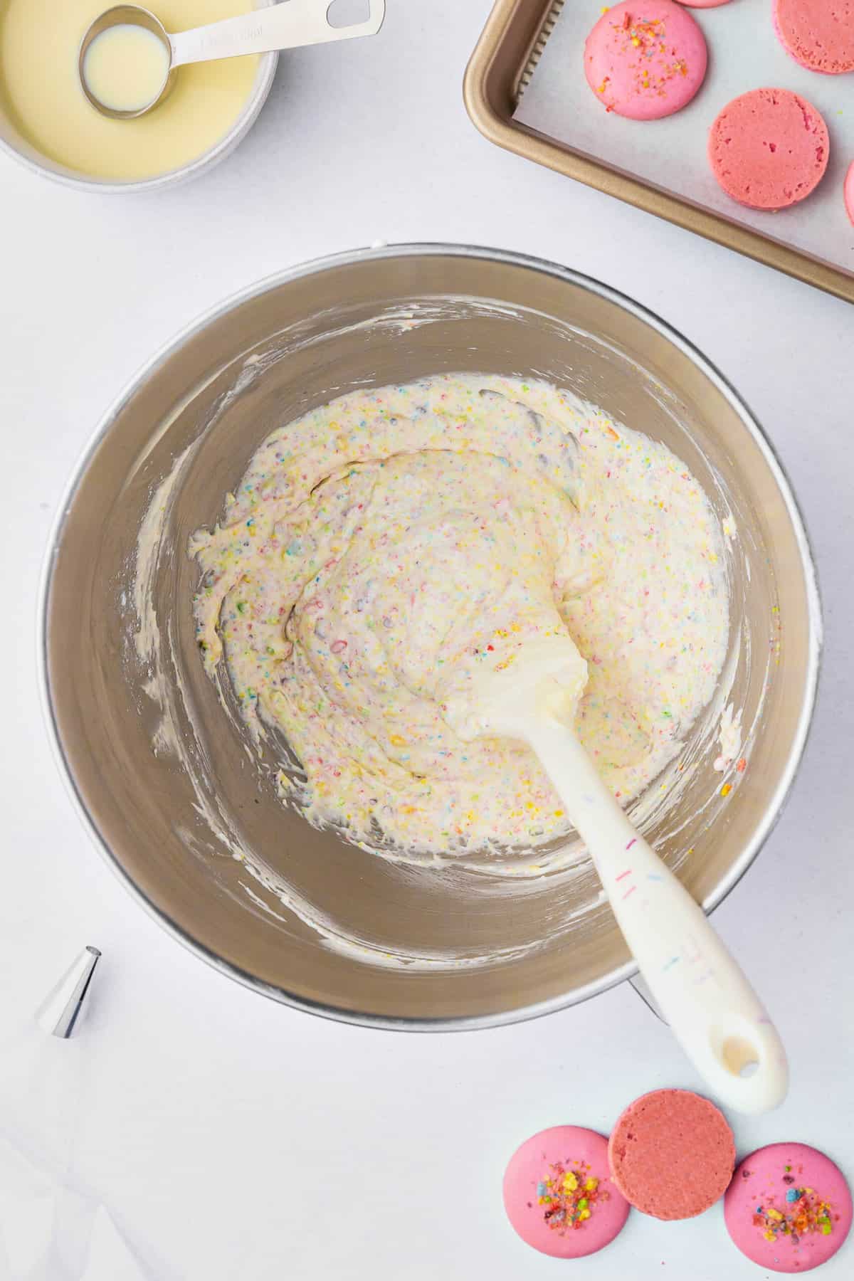 Mixing Fruity Pebbles buttercream frosting in a large metal bowl with a white spatula.