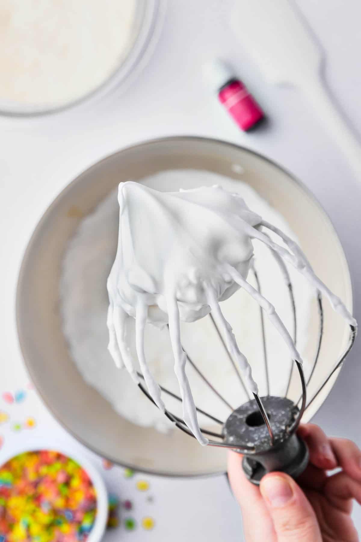 A whisk attachment holding up egg whites that have been whipped to stiff peaks.