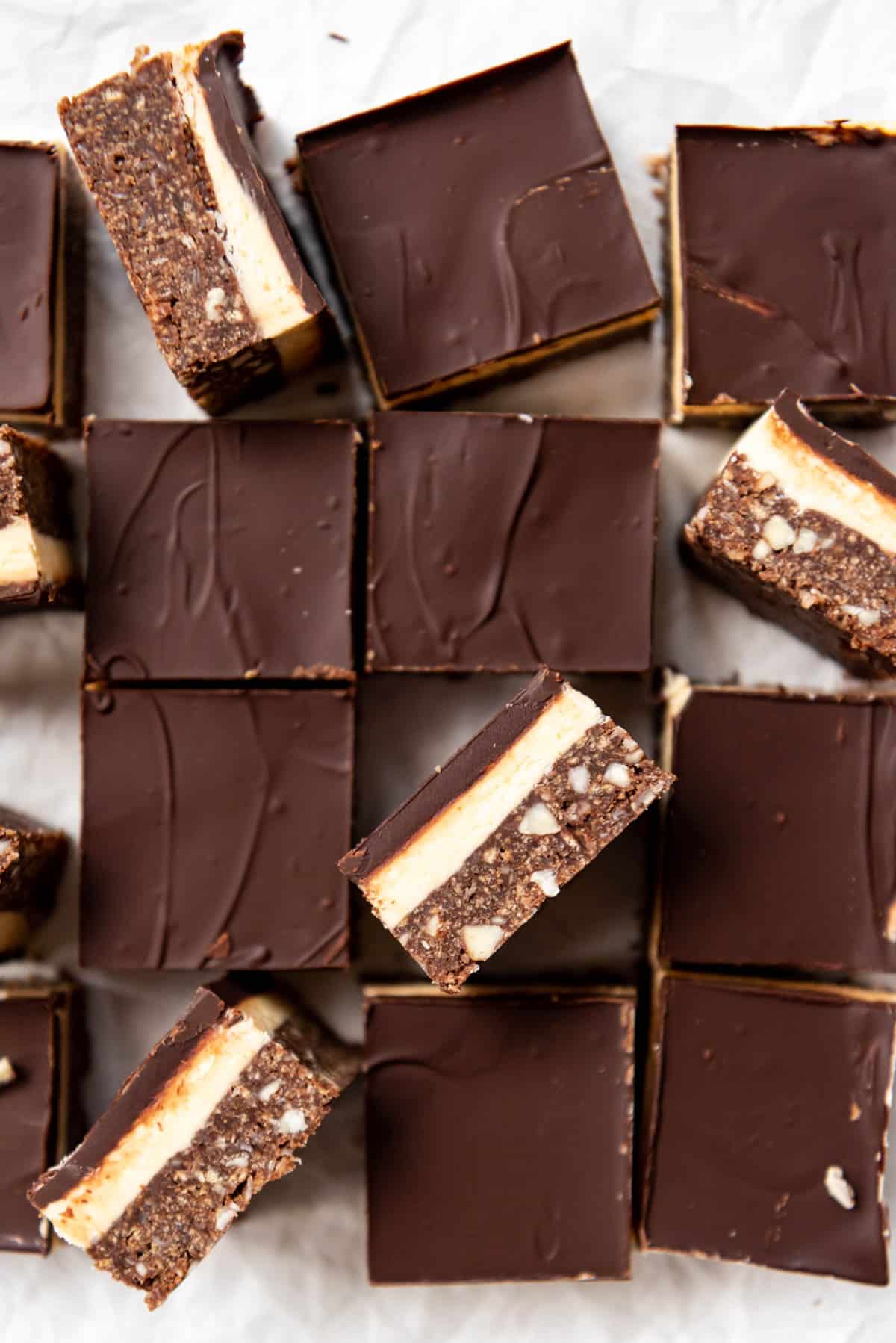 An overhead image of nanaimo bars that have been cut into squares with some standing on the sides to show the layers inside.