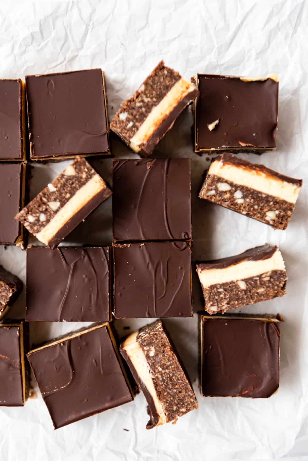 Nanaimo bar treats arranged haphazardly on crumpled white parchment paper.