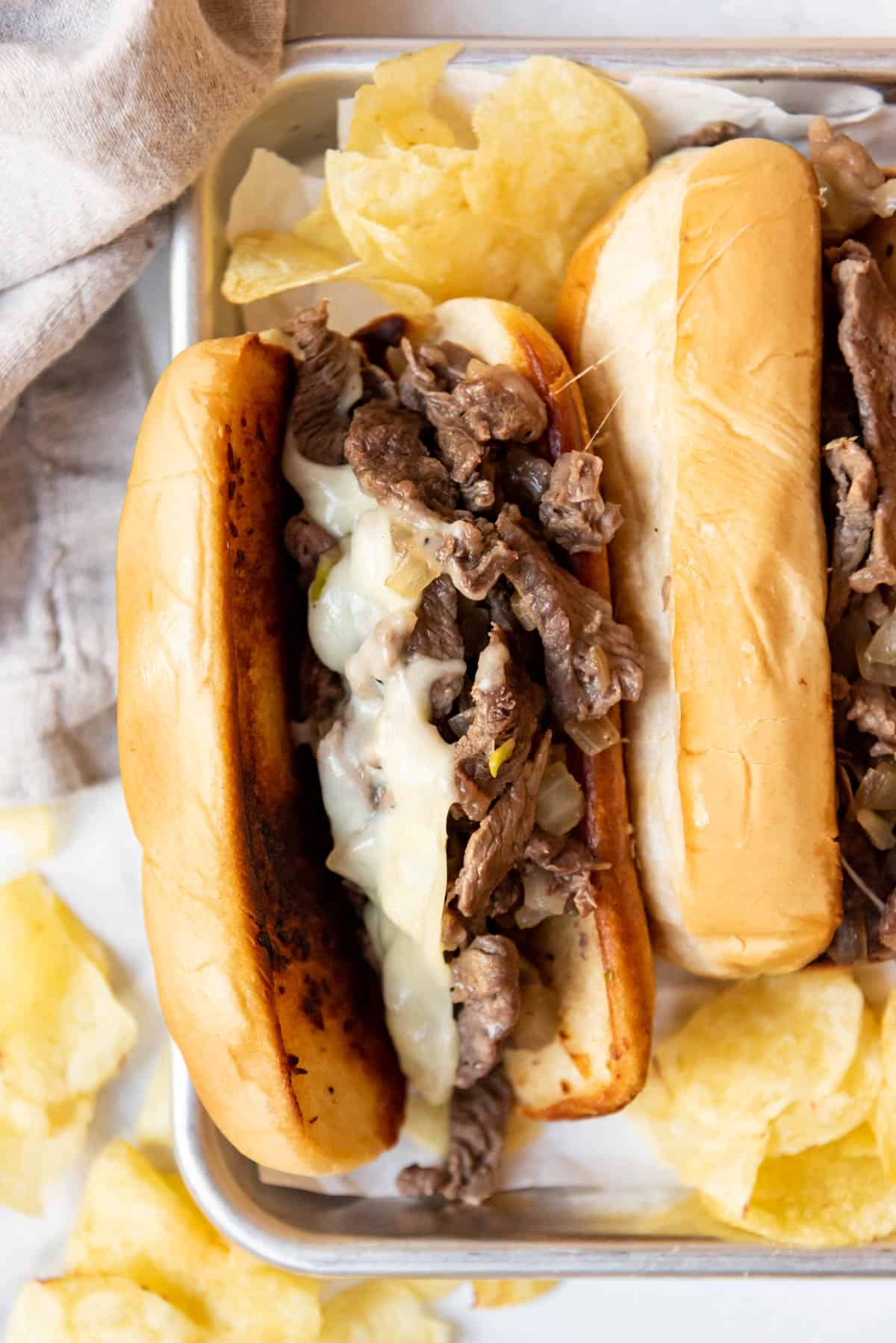 Philly cheese steak sandwiches next to potato chips.