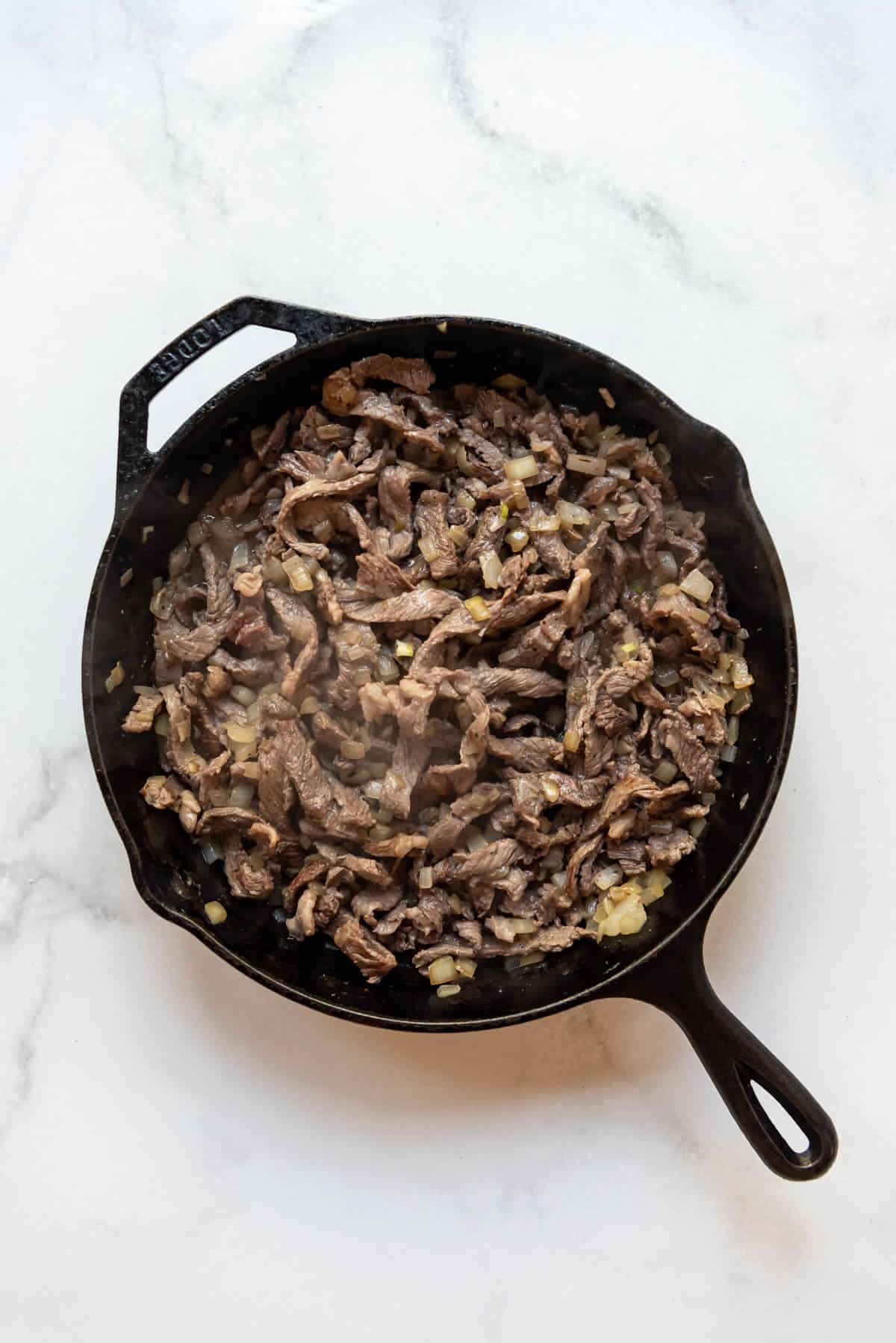 Cook philly cheese steak meat and onions in a pan.