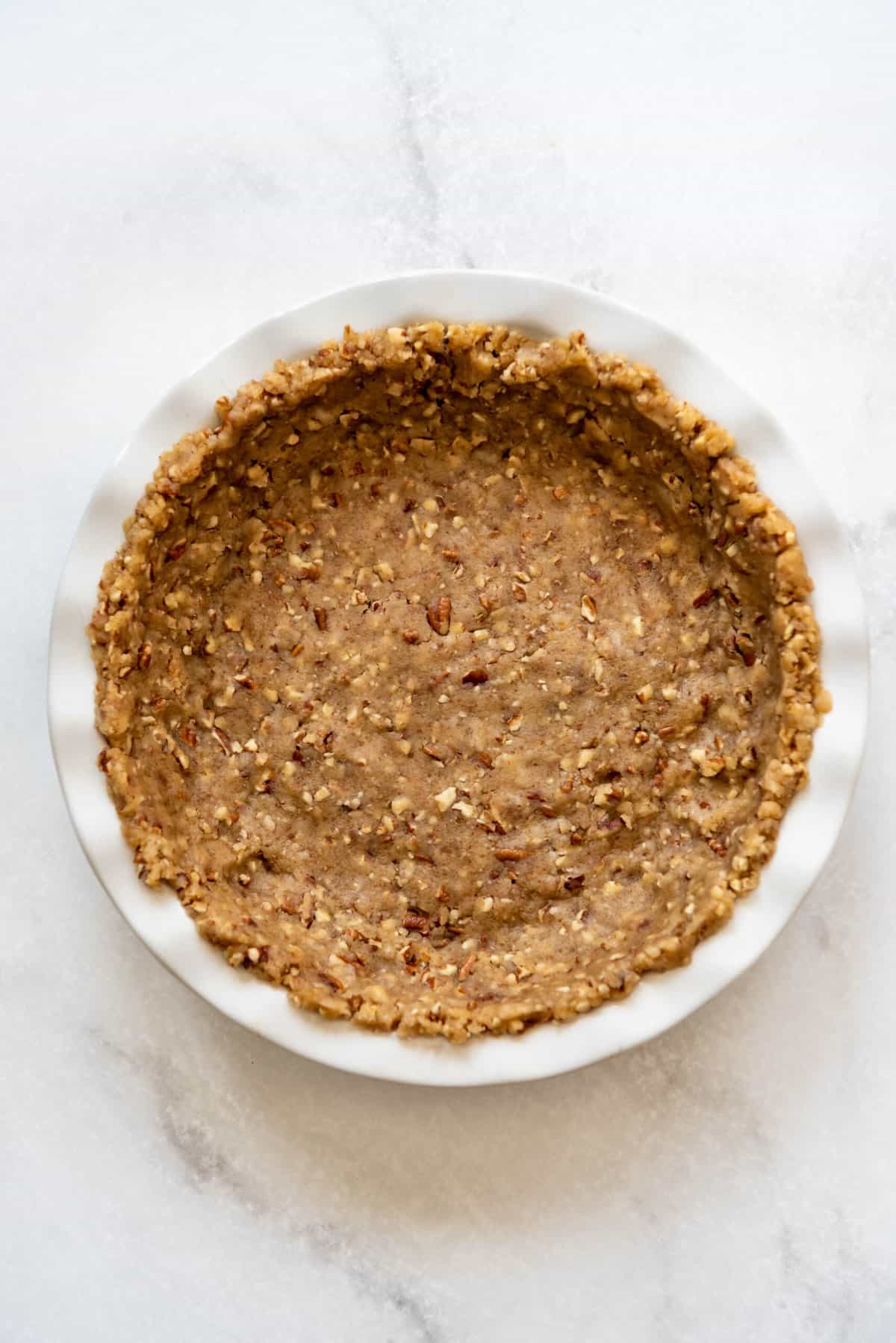 An image of a pecan pie crust for possum pie in a white baking dish.