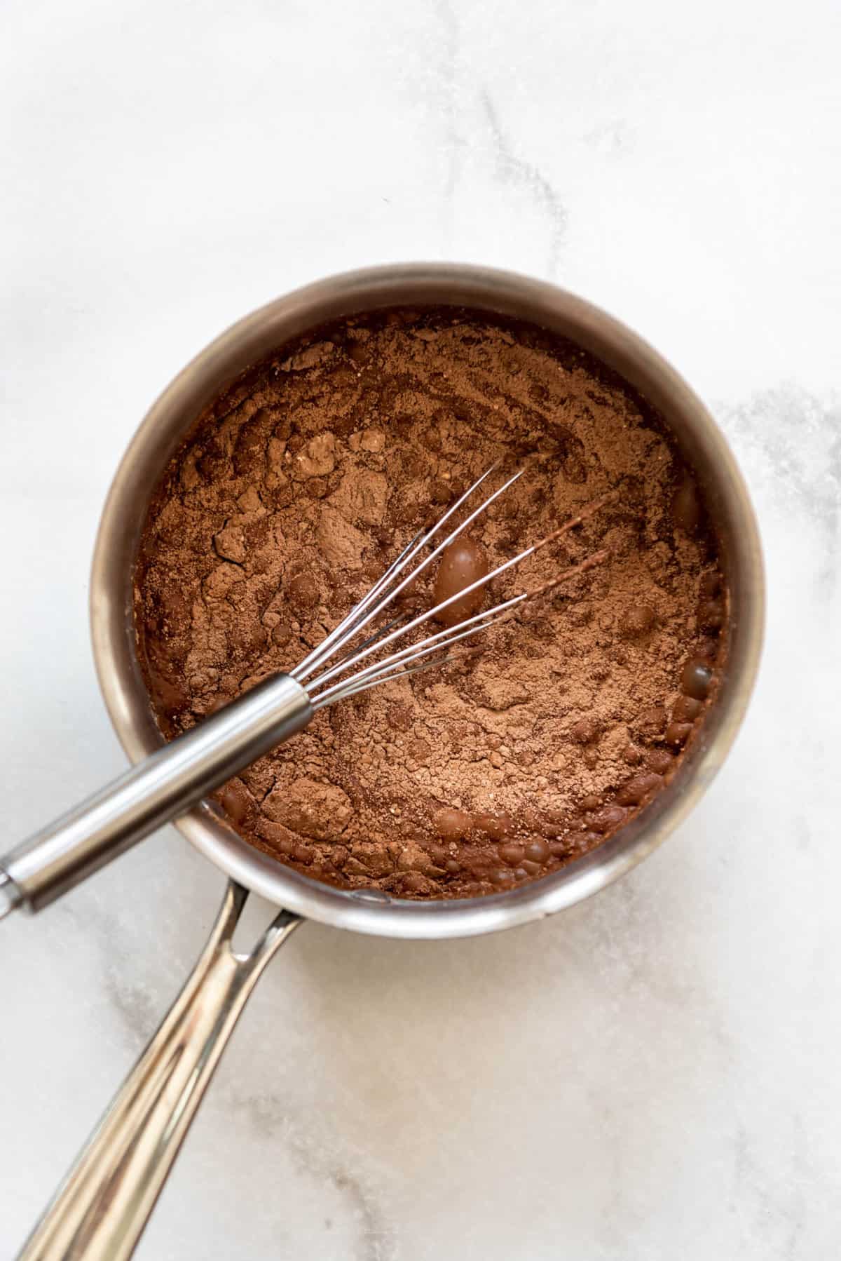 Whisking cocoa powder and cornstarch into milk and sugar to make chocolate pudding.