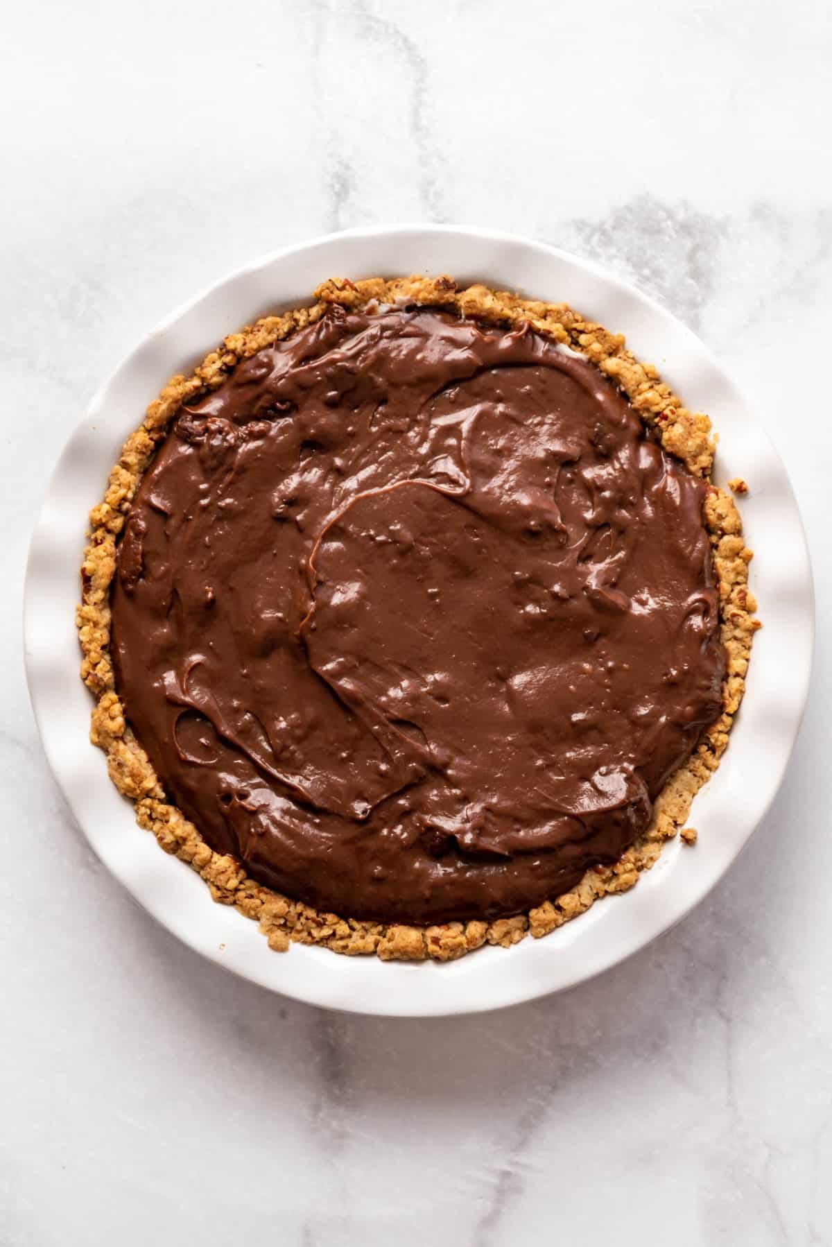 Adding a cooled chocolate pudding layer on top of a creamy layer in a pie crust.