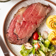 A slice of smoked prime rib roast on a plate with salad and duchess potatoes.