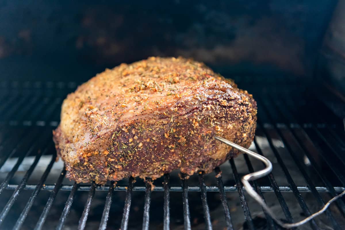 A ribeye roast on a smoker with a meat thermometer probe in it.